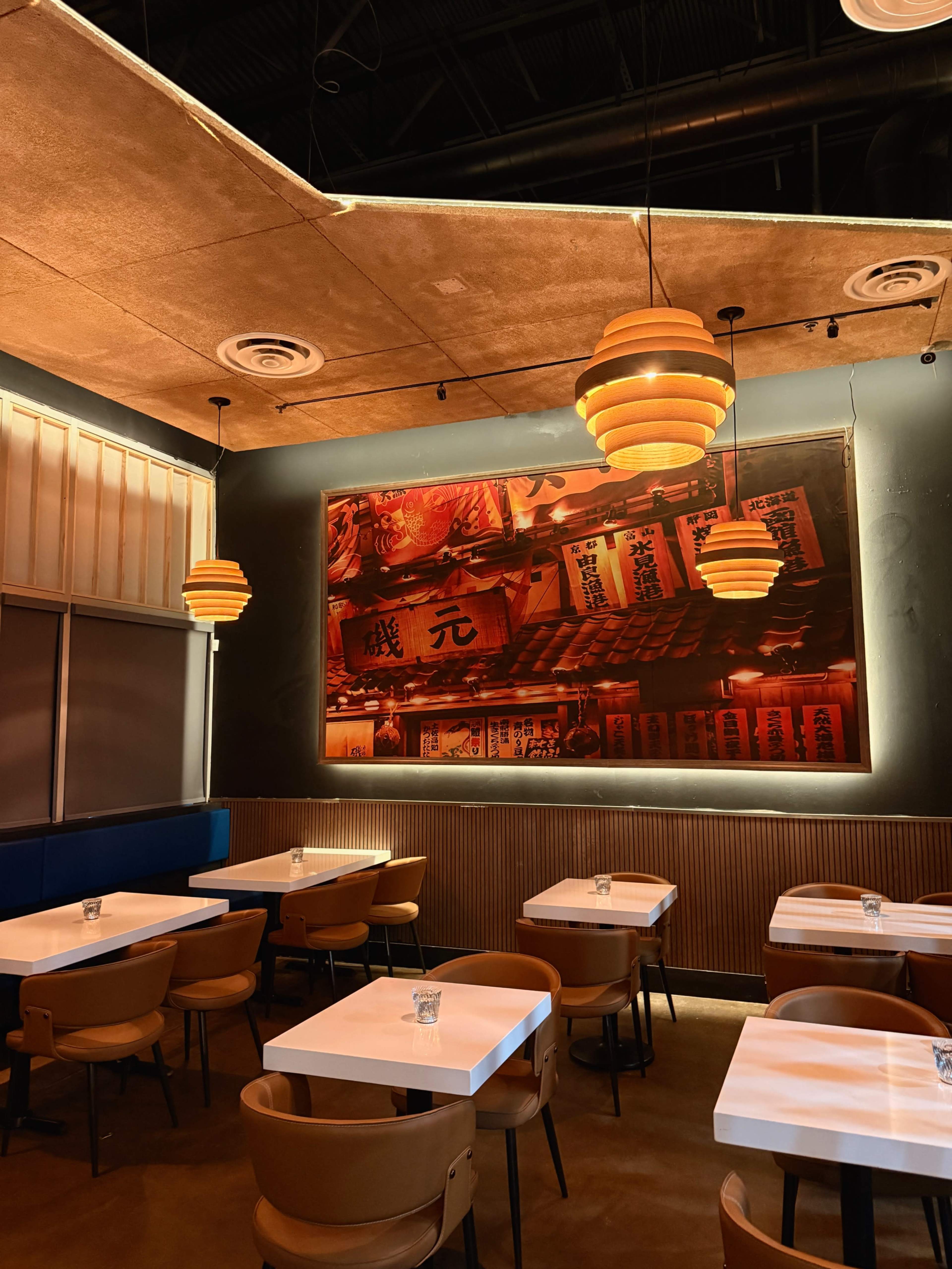 The image shows a modern restaurant interior with wooden ceiling panels, pendant lighting, and tables arranged beneath a large colorful mural.