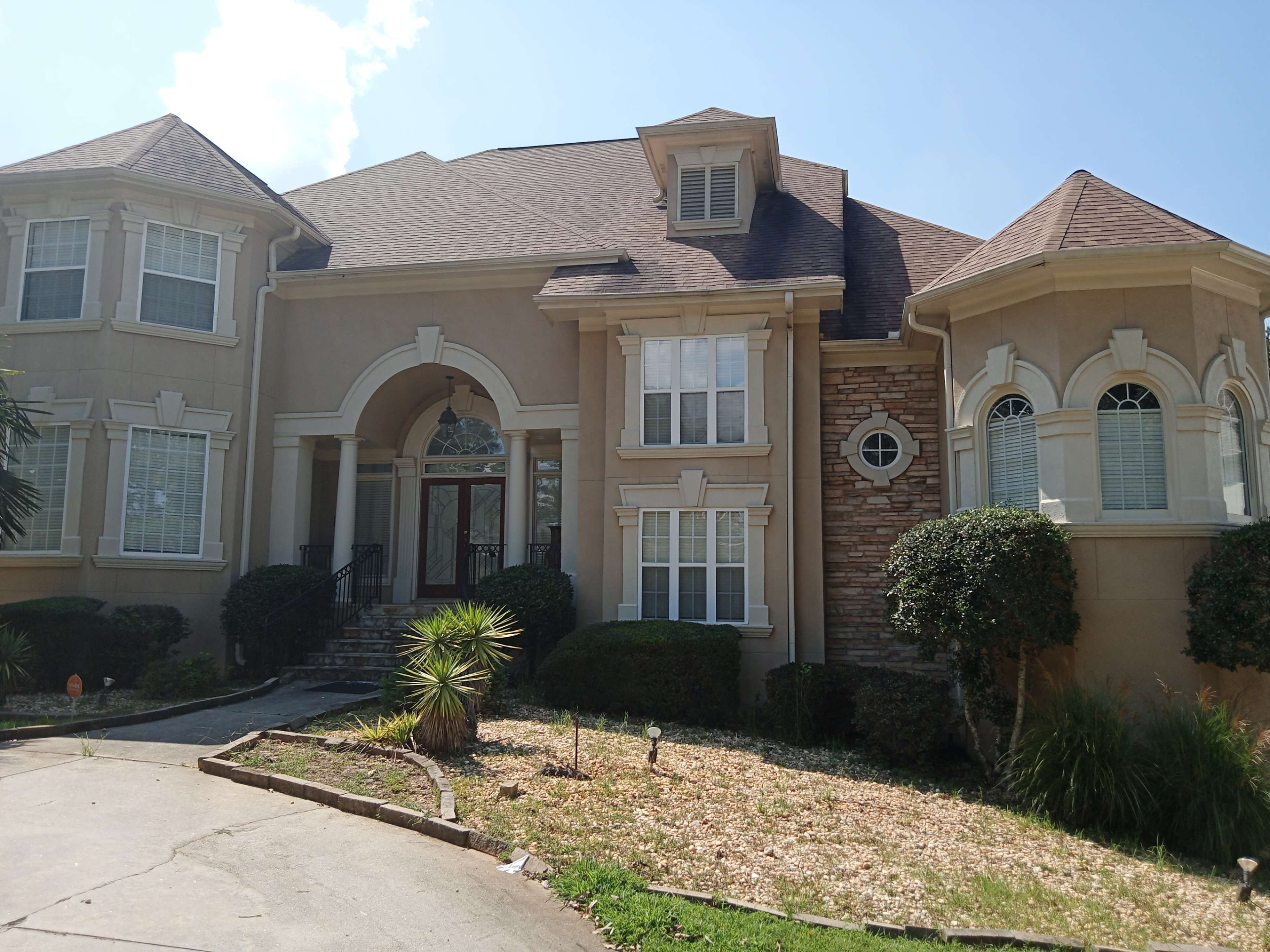 A large, two-story house with a mix of stone and stucco exterior, featuring a prominent entryway and multiple windows.