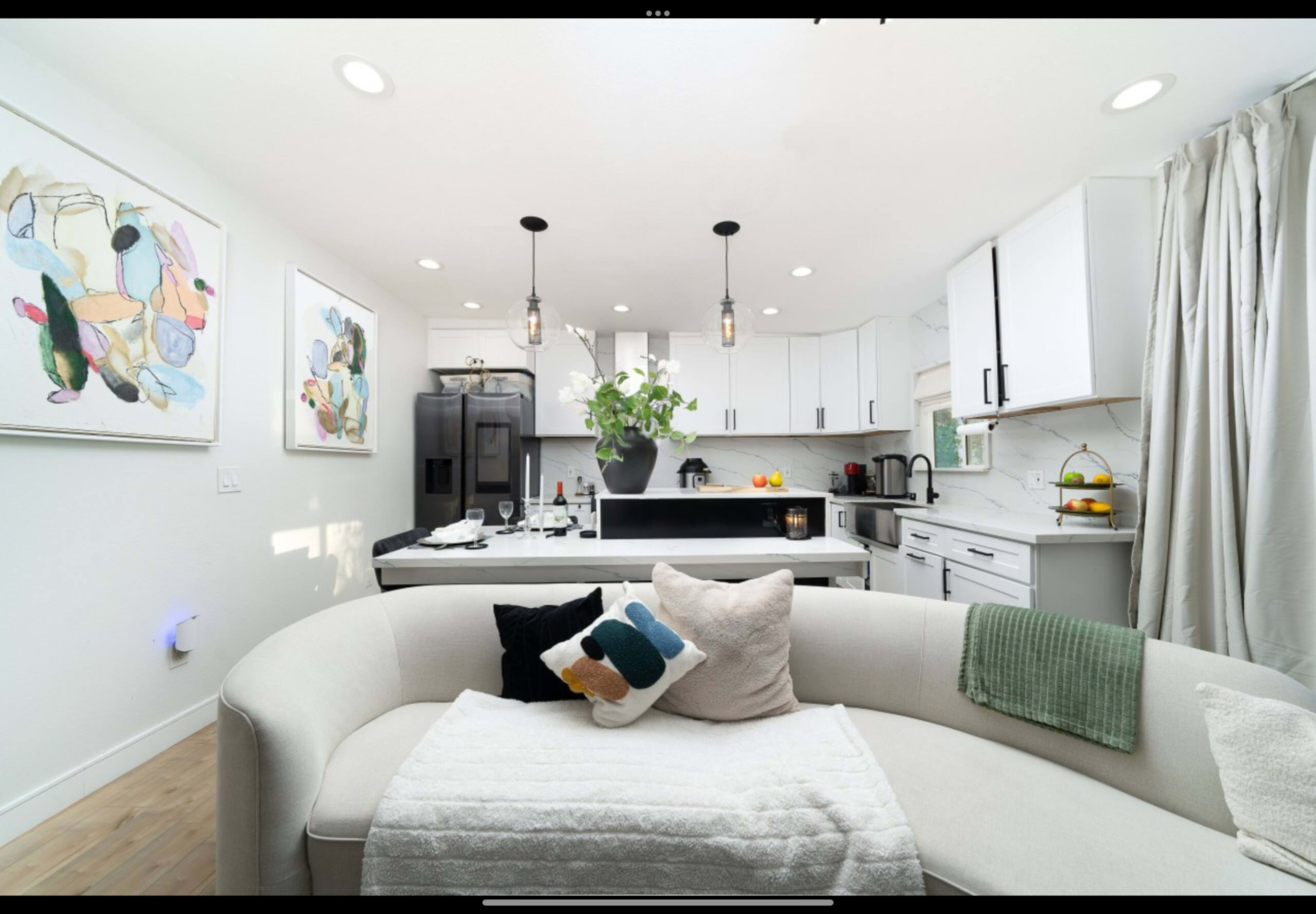 A modern kitchen and living area with a curved white sofa, dark cabinetry, and artwork on the walls.