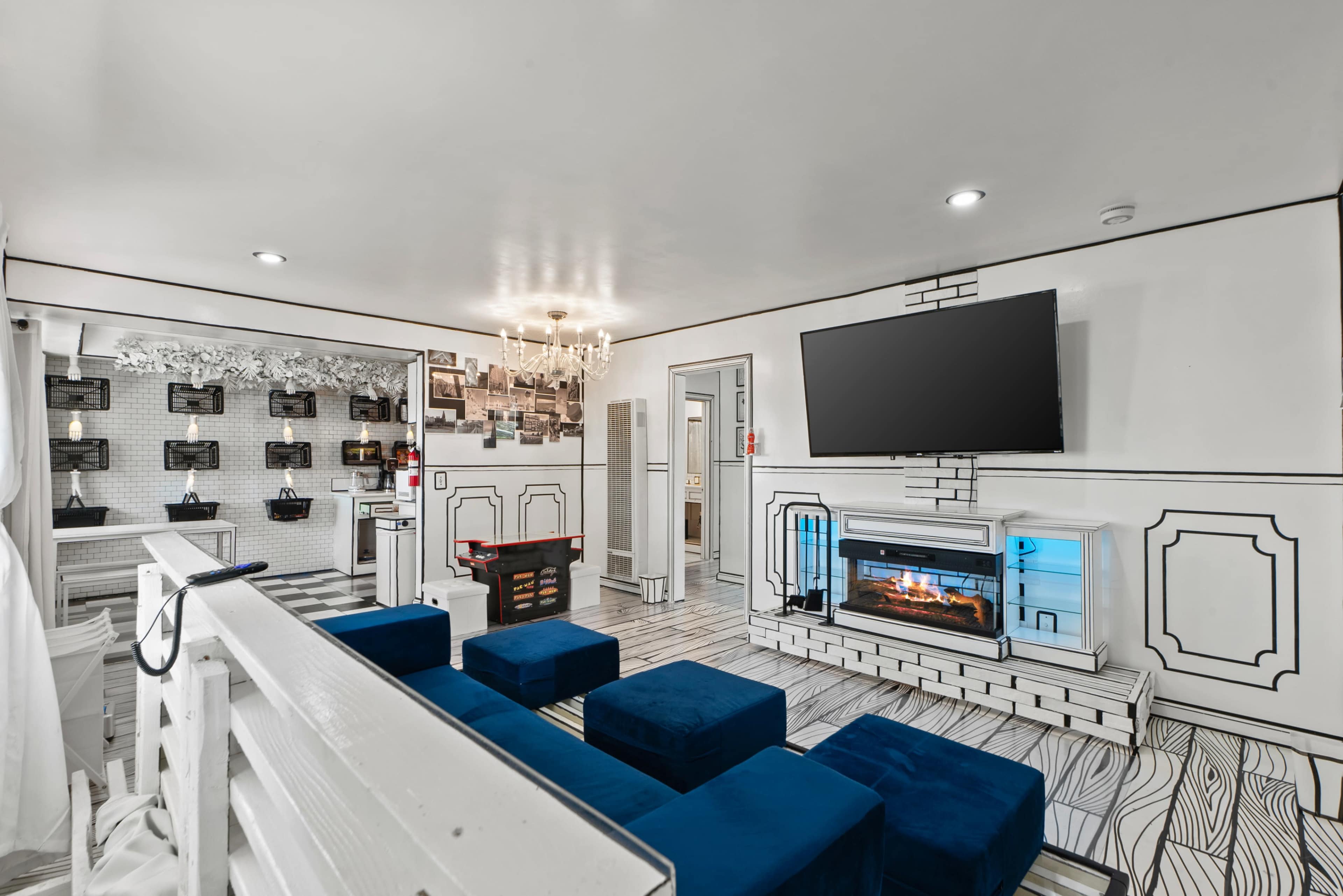 The image shows a modern living room with white walls, a television mounted on the wall, a fireplace, and blue seating.