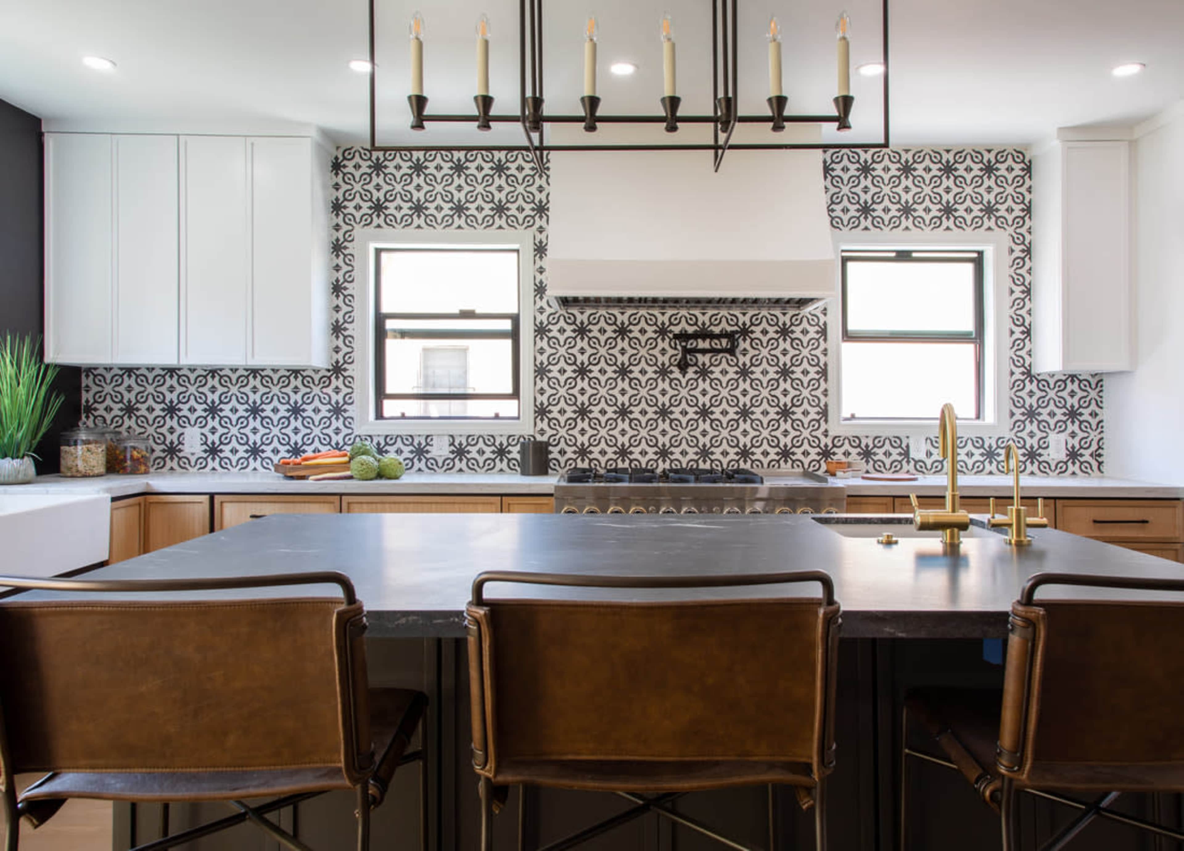 A modern kitchen with patterned tile backsplash, a large central island with barstools, and white cabinetry.