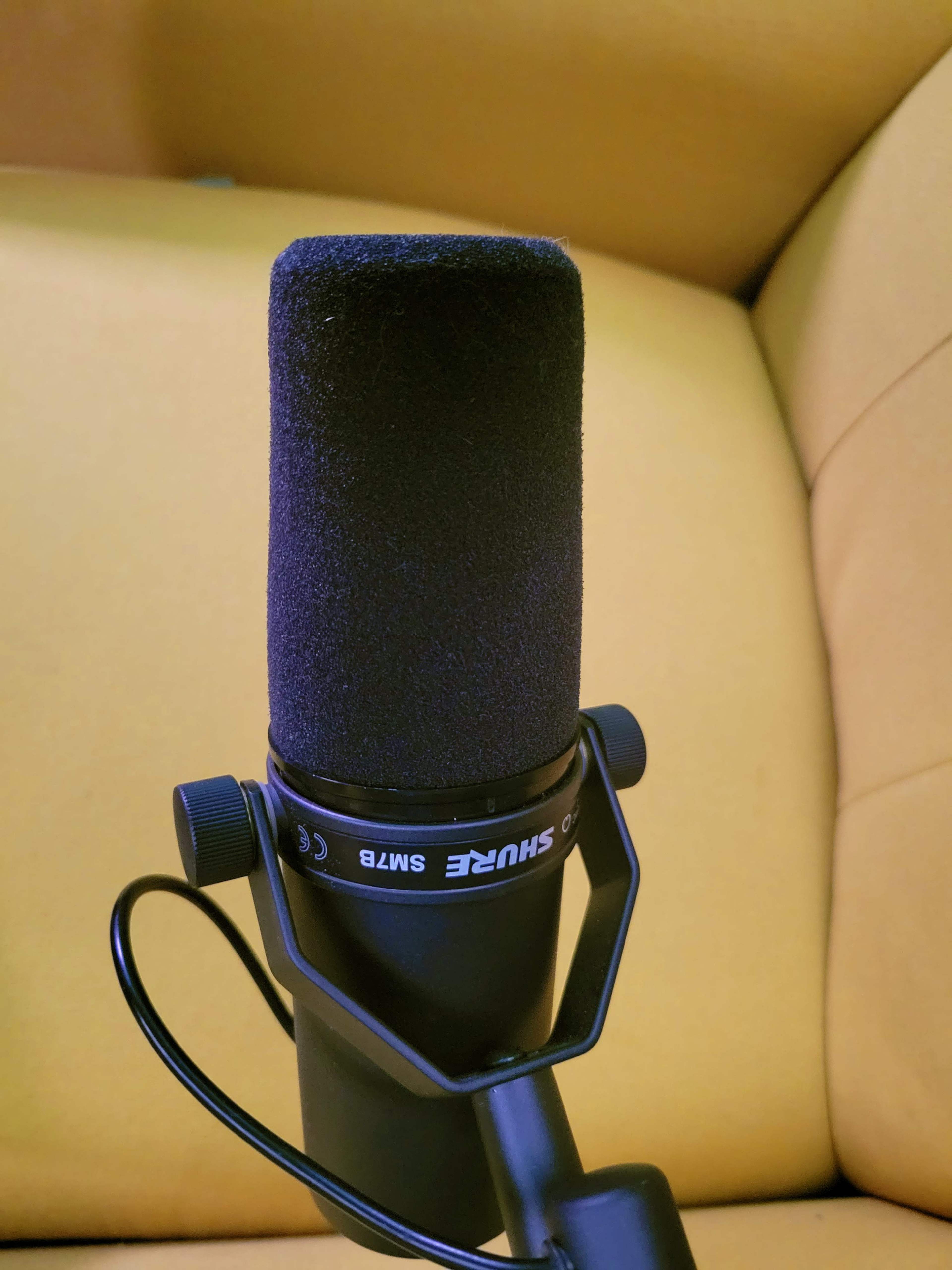 A black Shure SM7B microphone is positioned on a stand against a yellow background.