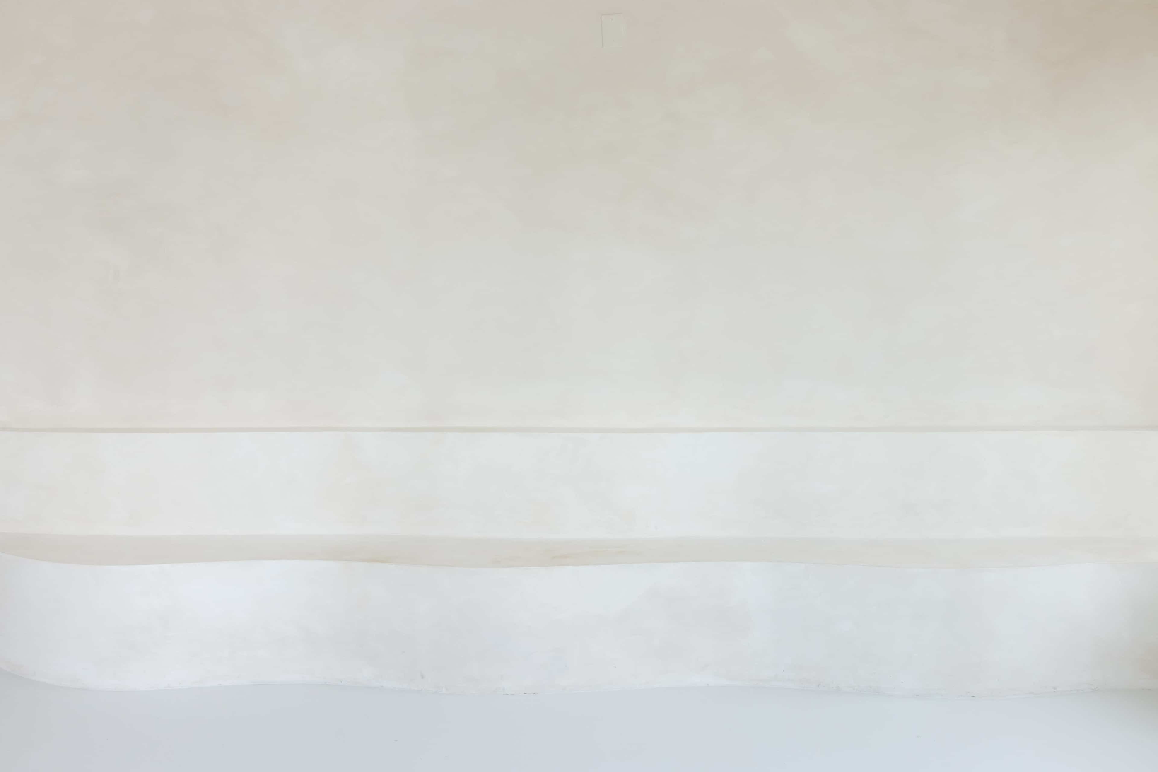The image shows a minimalistic, smooth, and light-colored wall with a curved bench at the bottom.