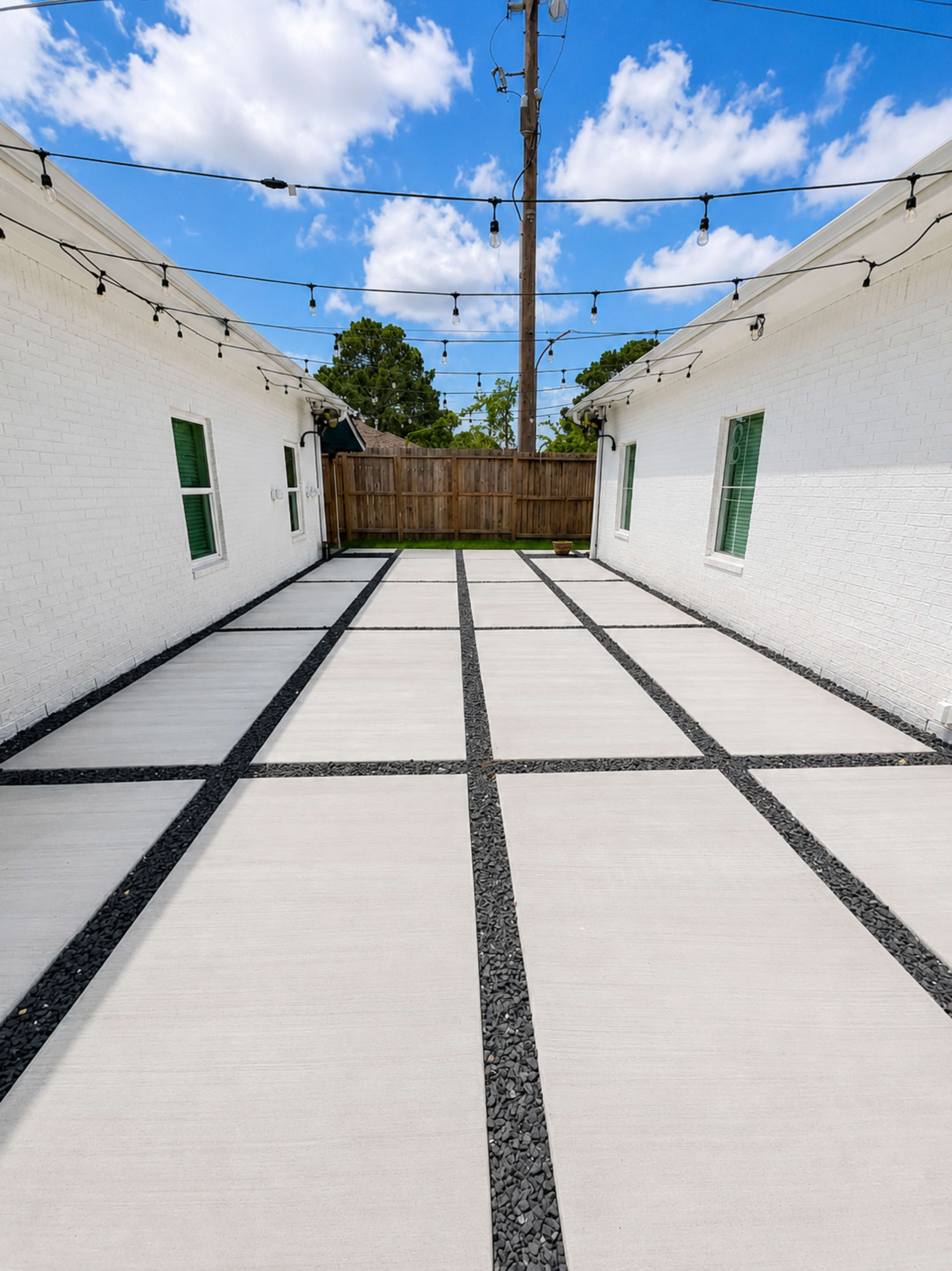 The image shows a spacious, neatly paved outdoor area between two white buildings, with a grid pattern of concrete slabs and black gravel outlining the spaces.