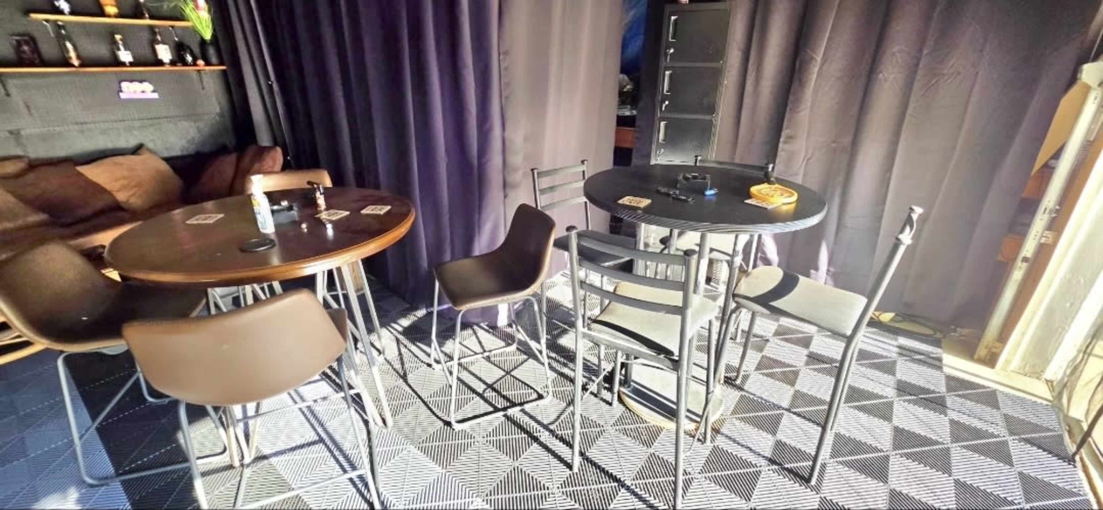 The image displays a small indoor space featuring two tables with chairs, surrounded by dark curtains and a patterned floor.