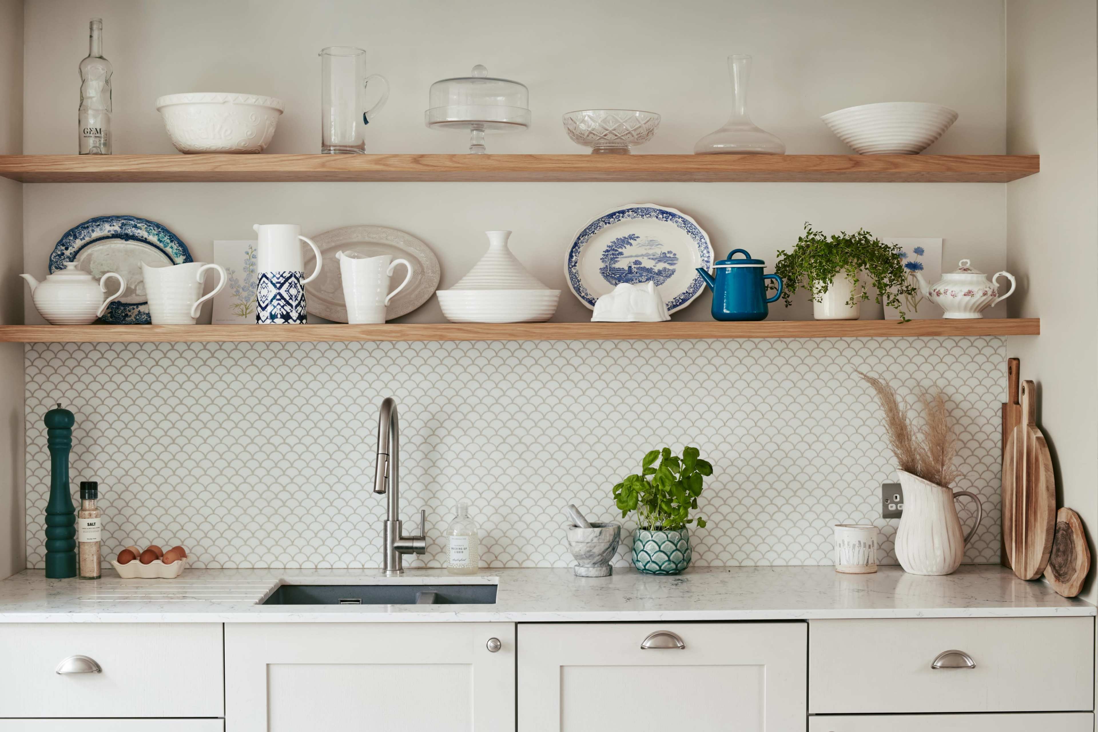 A modern kitchen features open shelves adorned with various dishes and decorative items above a sink with a marble countertop.