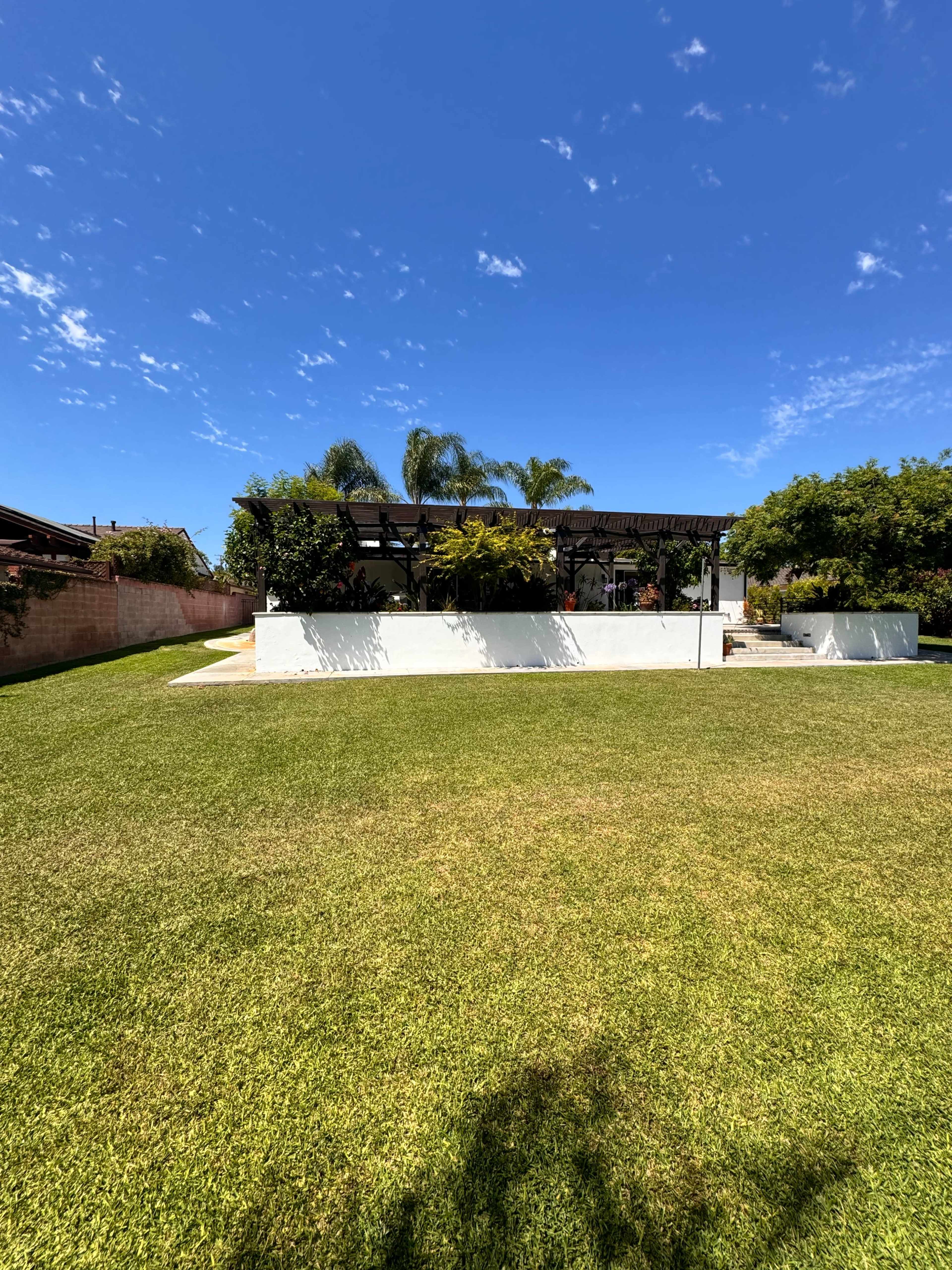 A white house with a patio and surrounding greenery is set against a blue sky with scattered clouds.