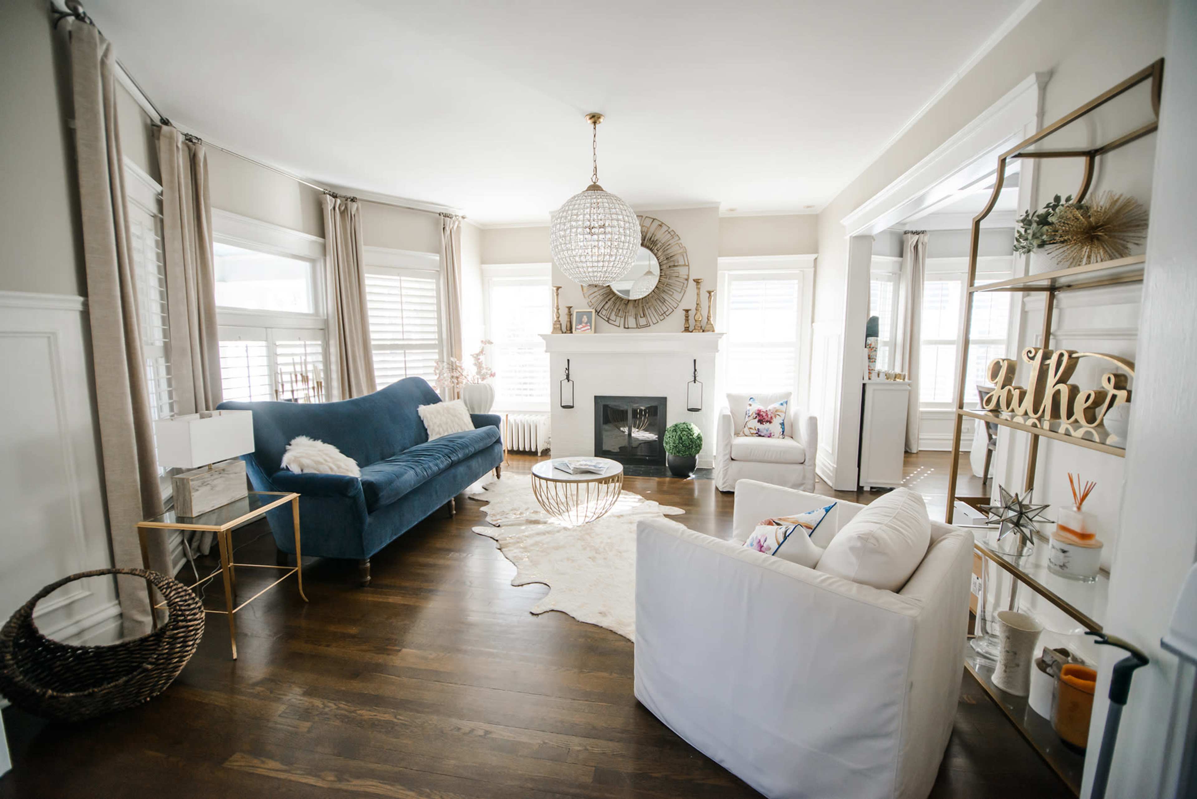 A modern living room features a blue sofa, white chairs, a round coffee table, a decorative rug, and a chandelier.
