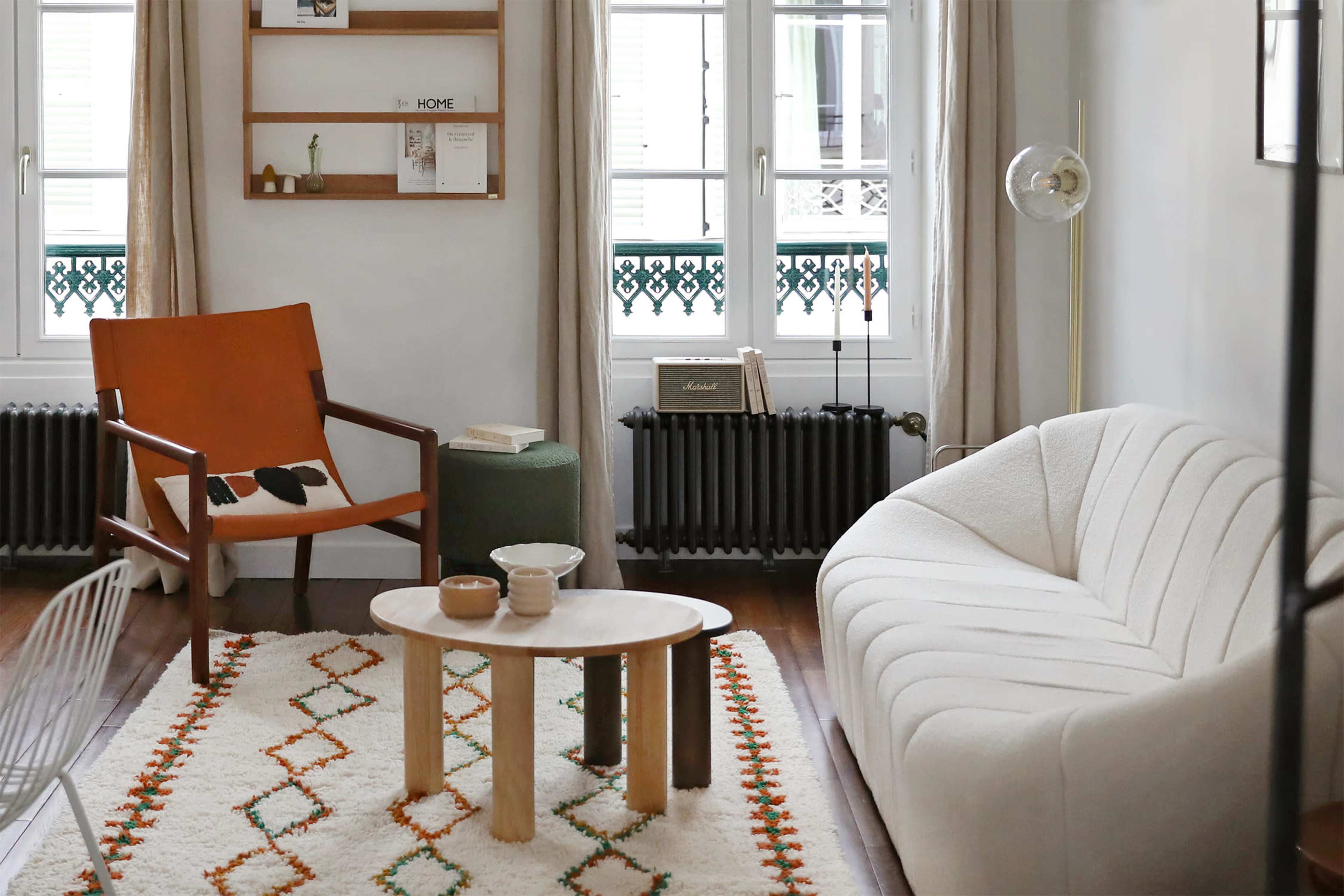 A modern living room featuring a white sofa, an orange armchair, a wooden coffee table, and a textured rug with geometric patterns.