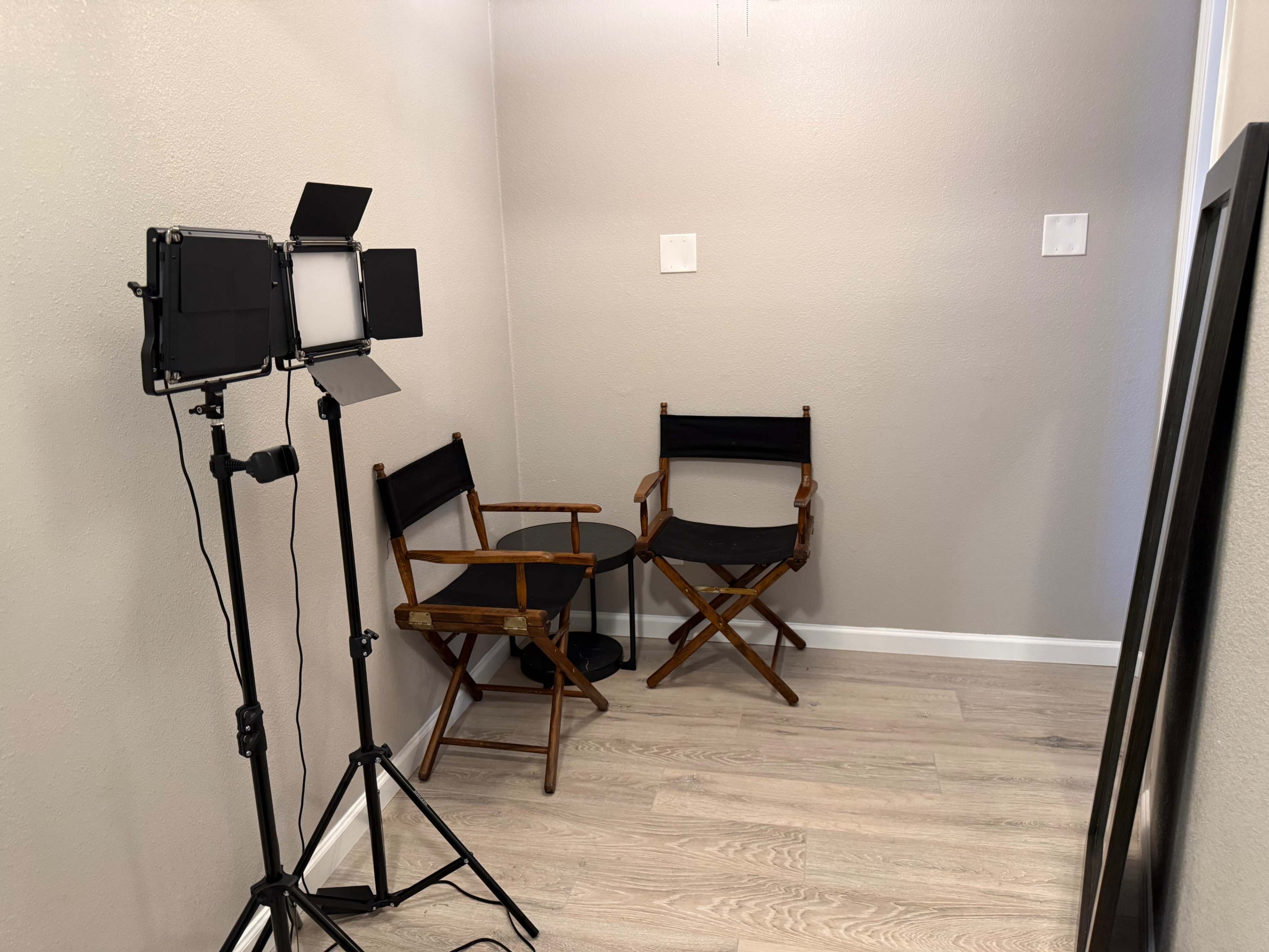 The image shows a small room featuring two folding chairs and a lighting setup on a stand.