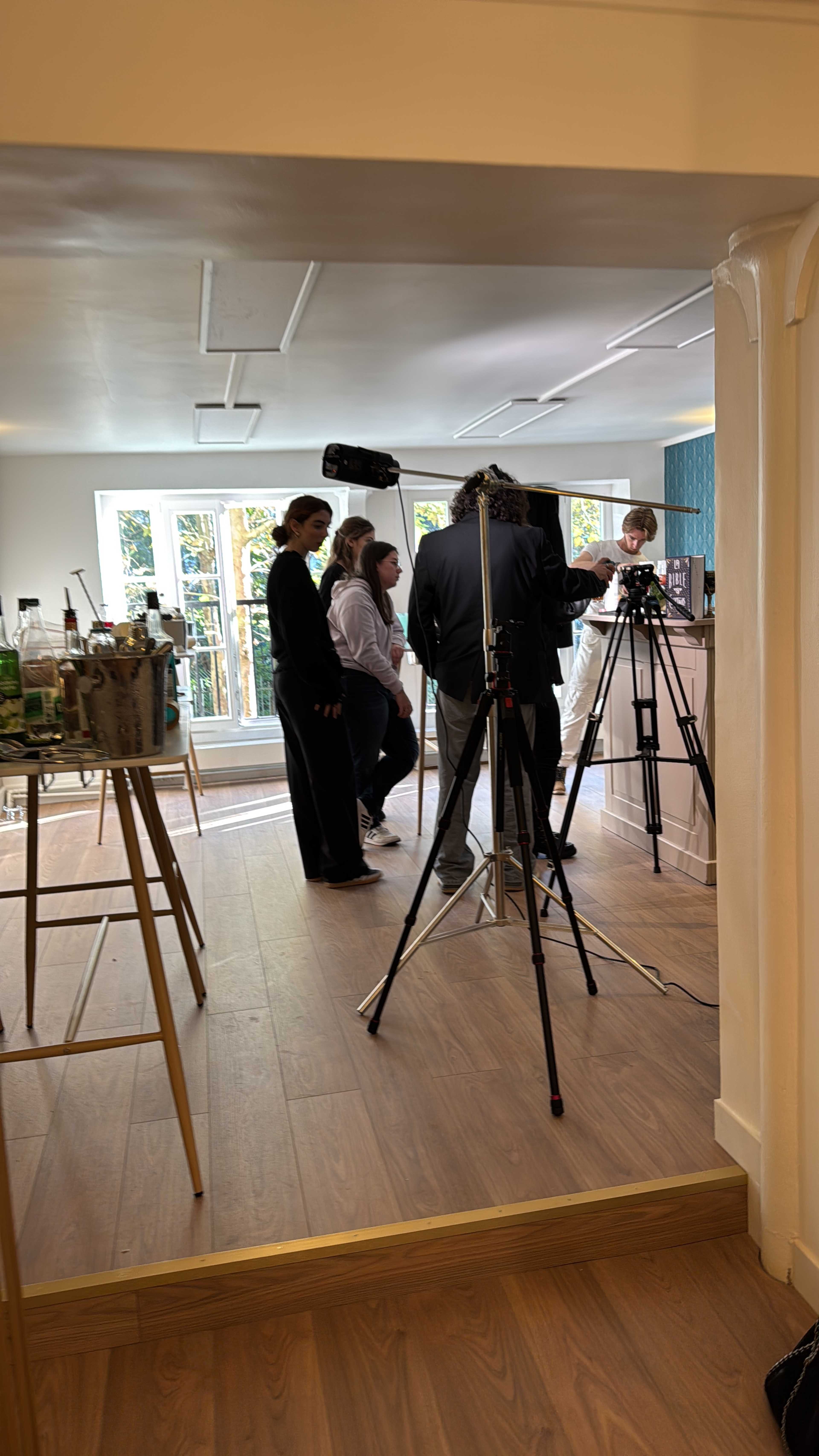 A group of people are gathered in a well-lit room with multiple cameras on tripods, as they prepare for a filming session.