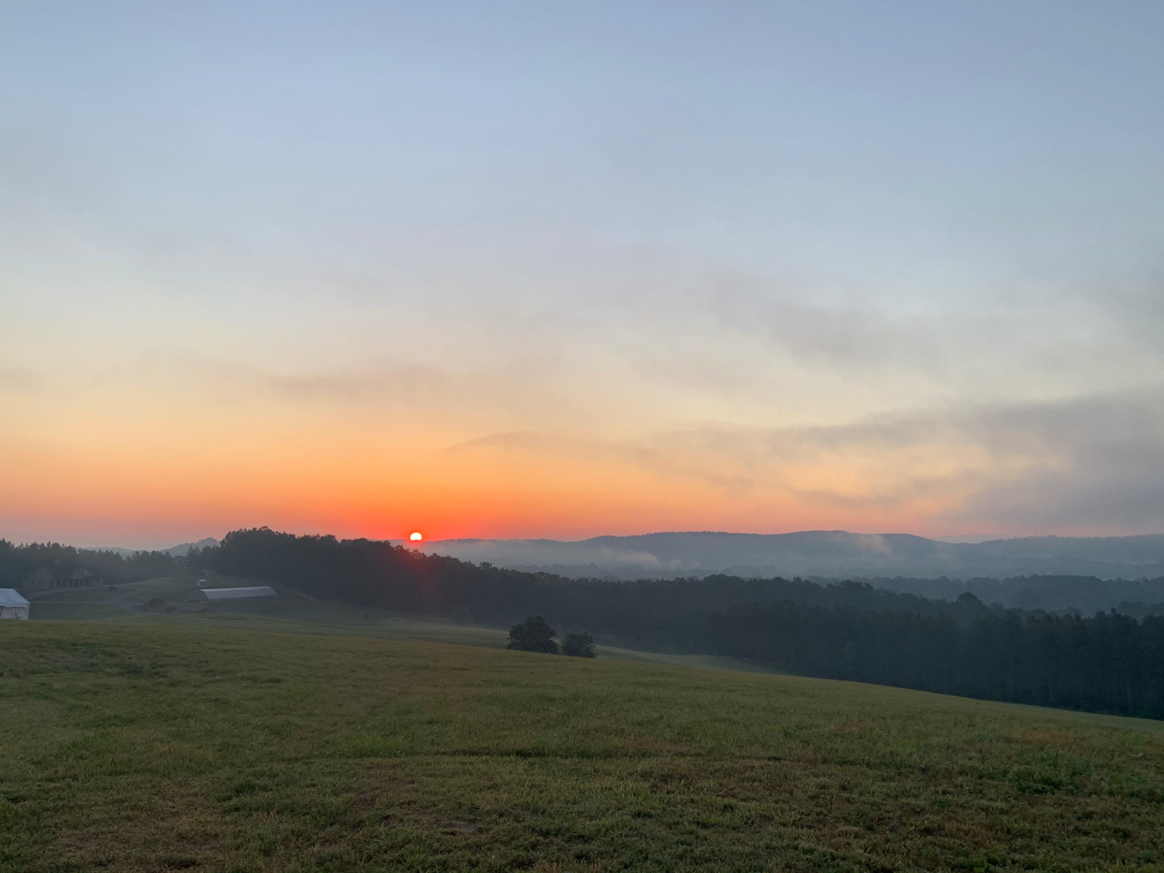 A sunrise casts a soft light over a green field and distant hills.