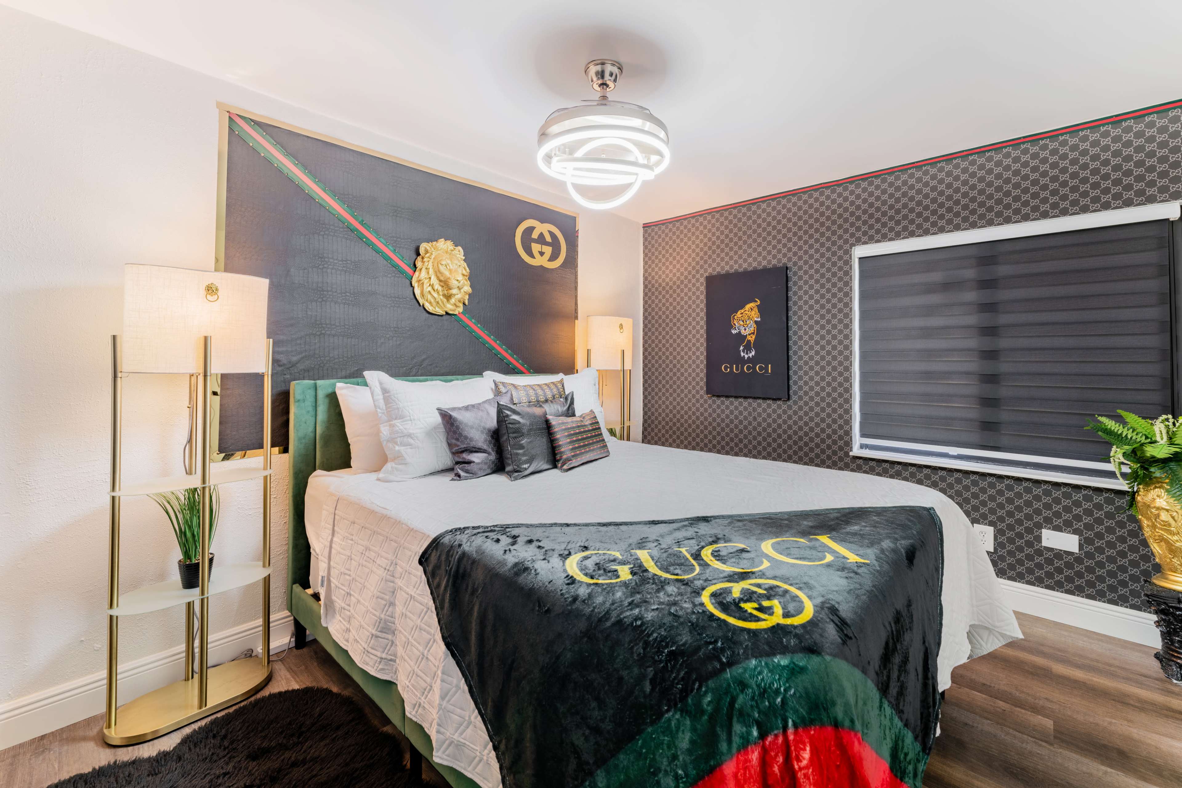The bedroom features a large bed covered with a black Gucci blanket, decorative wall art, and modern lighting.