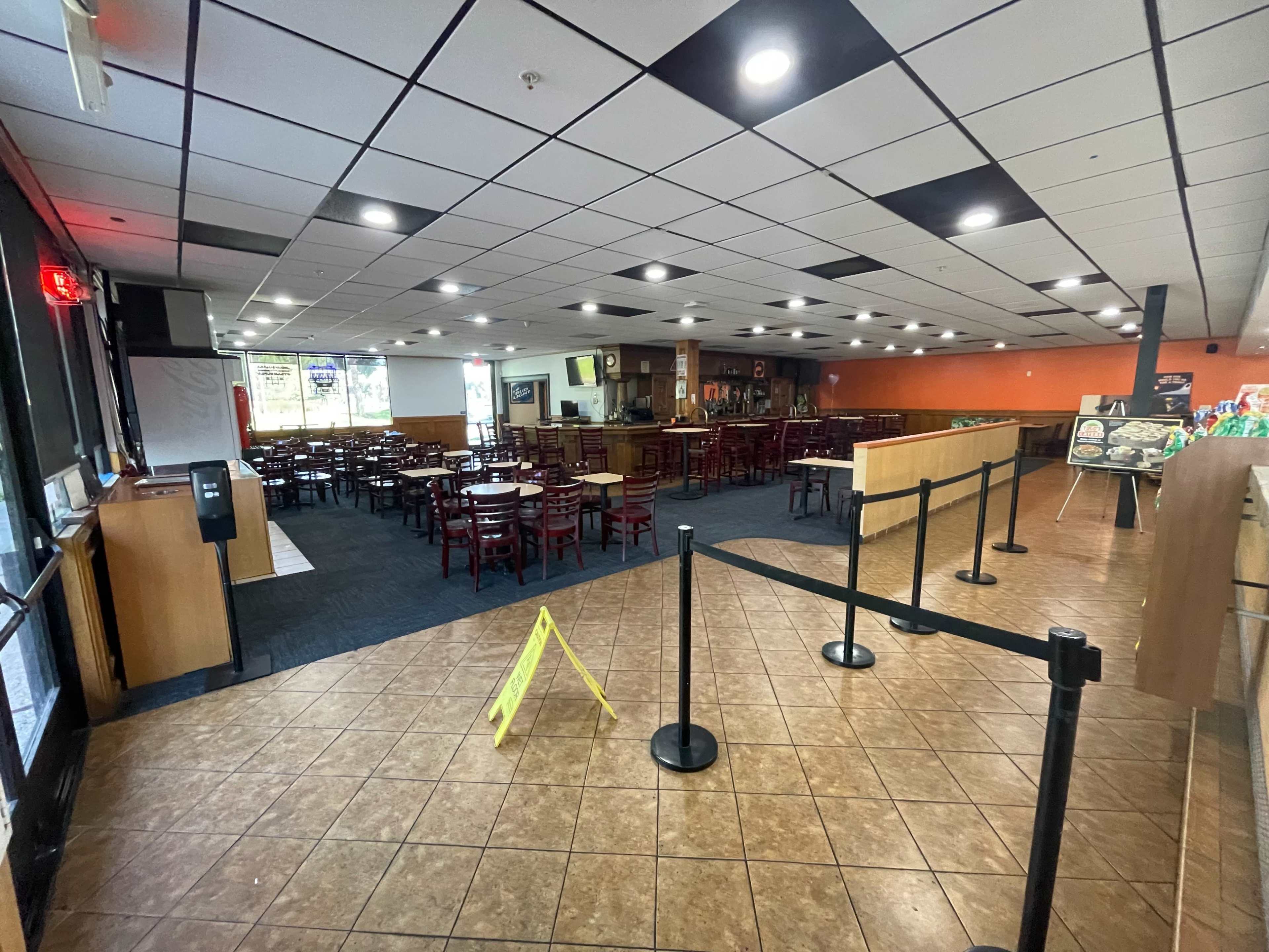 A largely empty restaurant interior with rows of chairs and tables, a cash register area, and caution signage on the floor.
