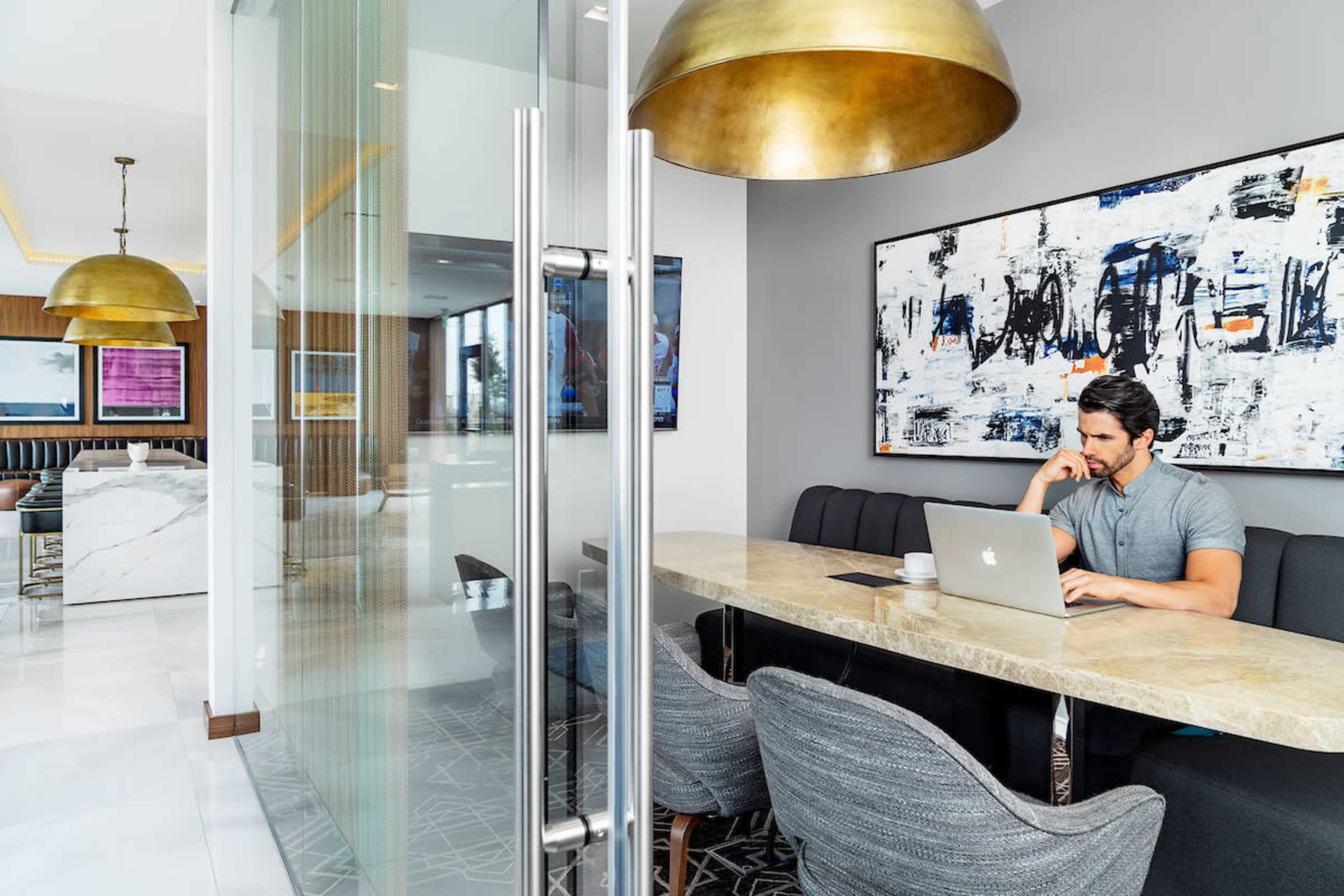 A man works on a laptop at a long marble table in a modern office space with contemporary artwork on the walls.