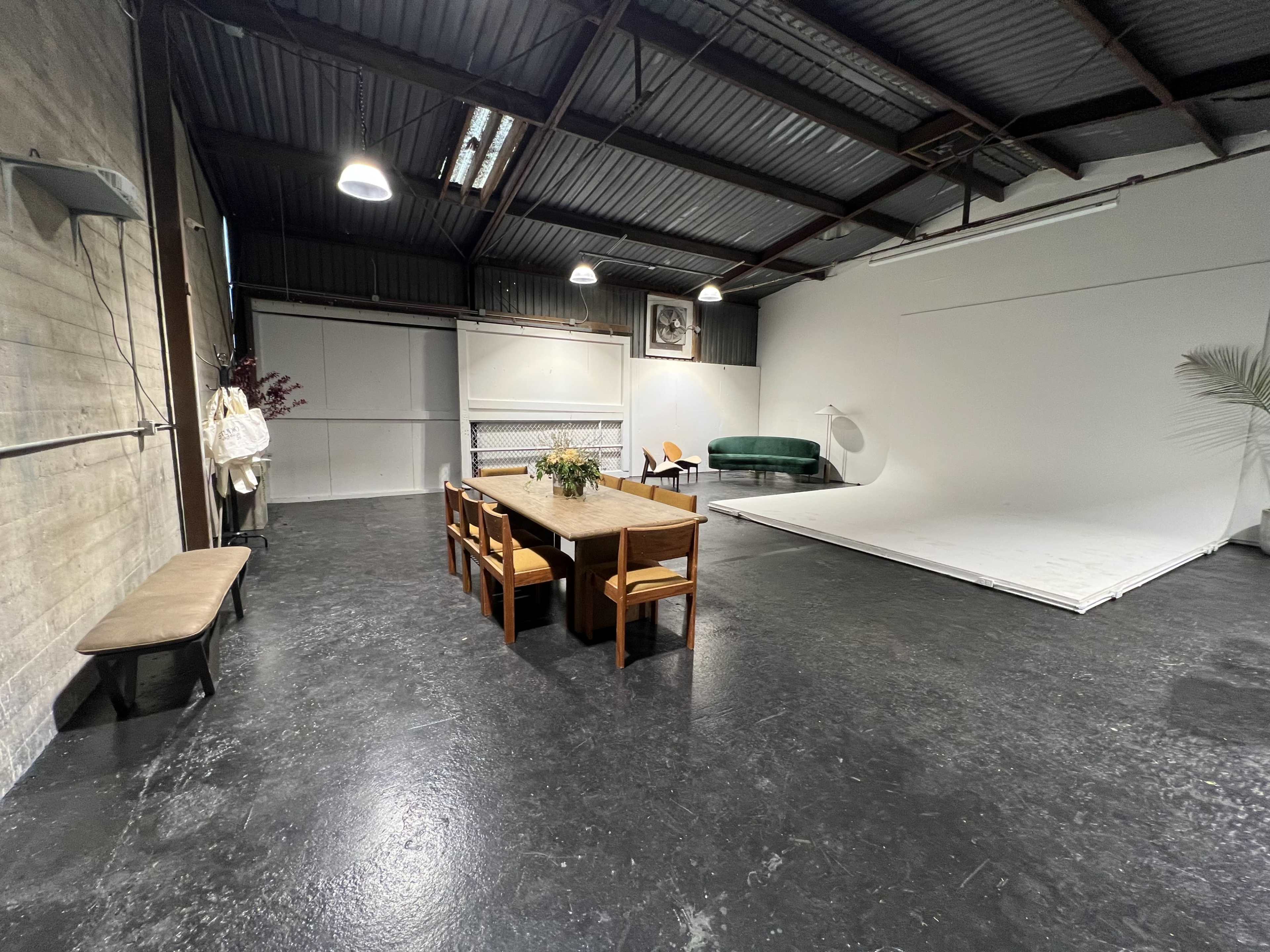 A spacious interior with a wooden dining table and chairs, a green couch, a photography backdrop, and overhead lighting.