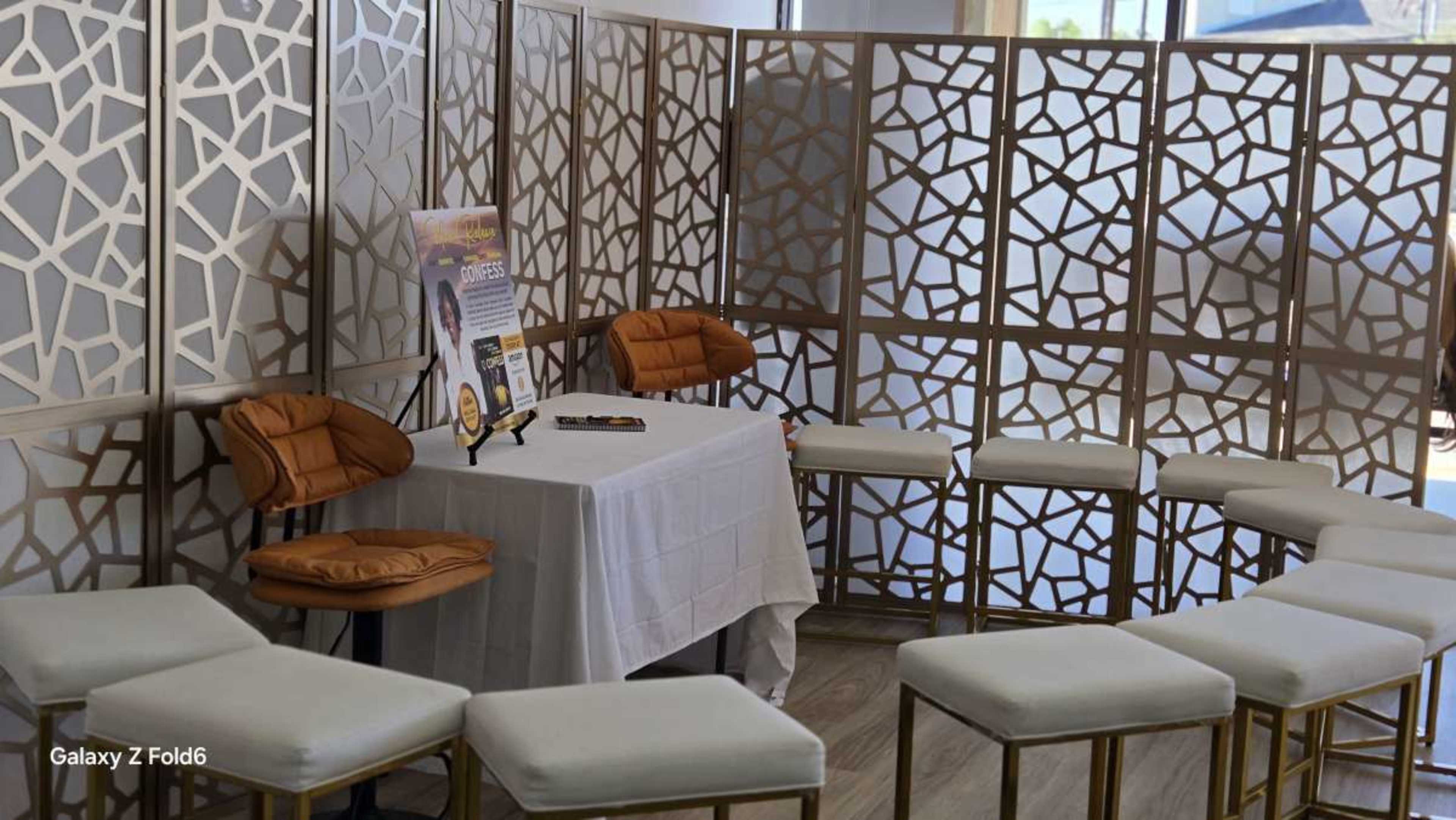 The image shows a small conference setup with four chairs around a table covered by a white cloth, framed by decorative partition panels.