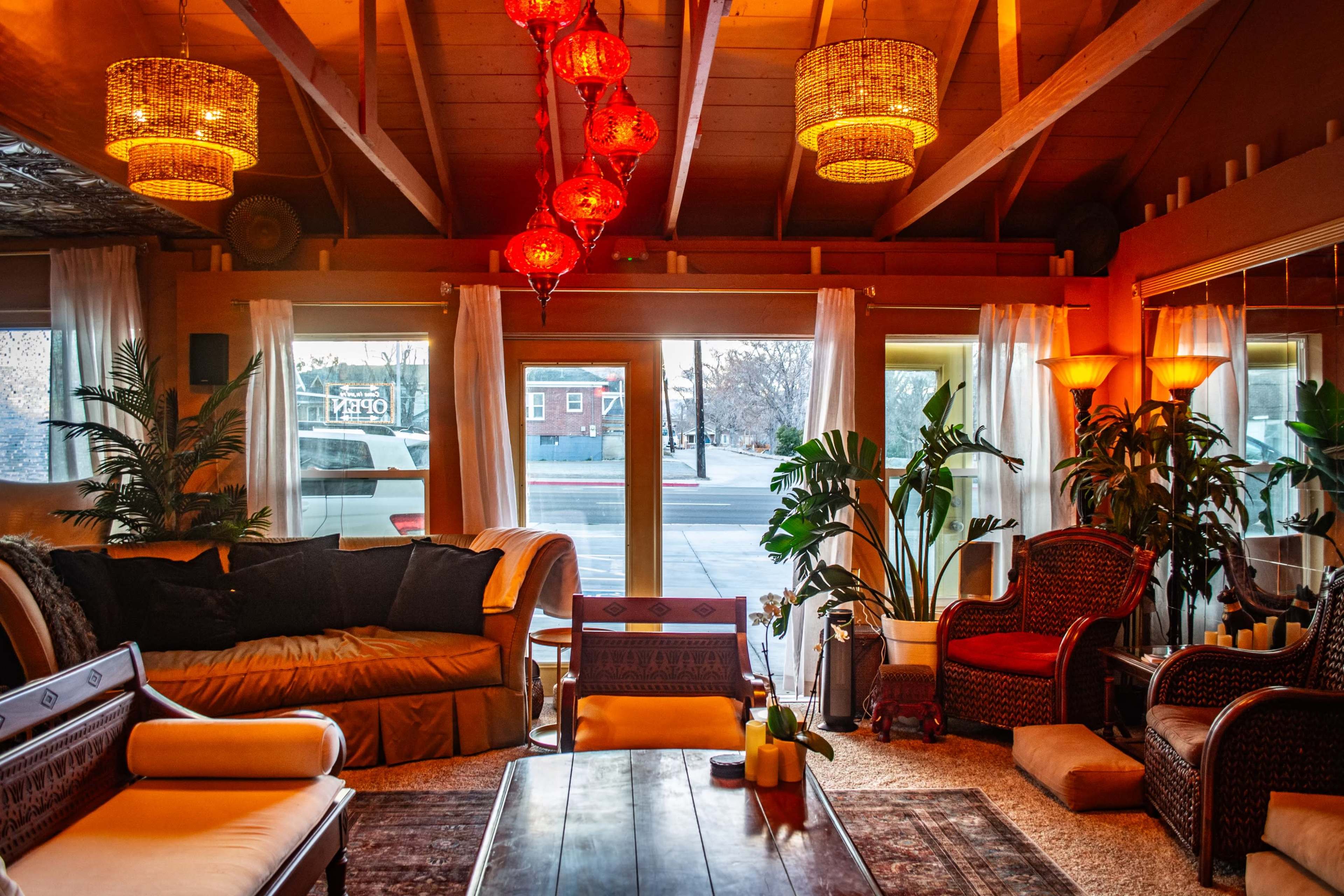 The image shows a cozy living room with a large sofa, wooden furniture, plants, and decorative hanging lights.