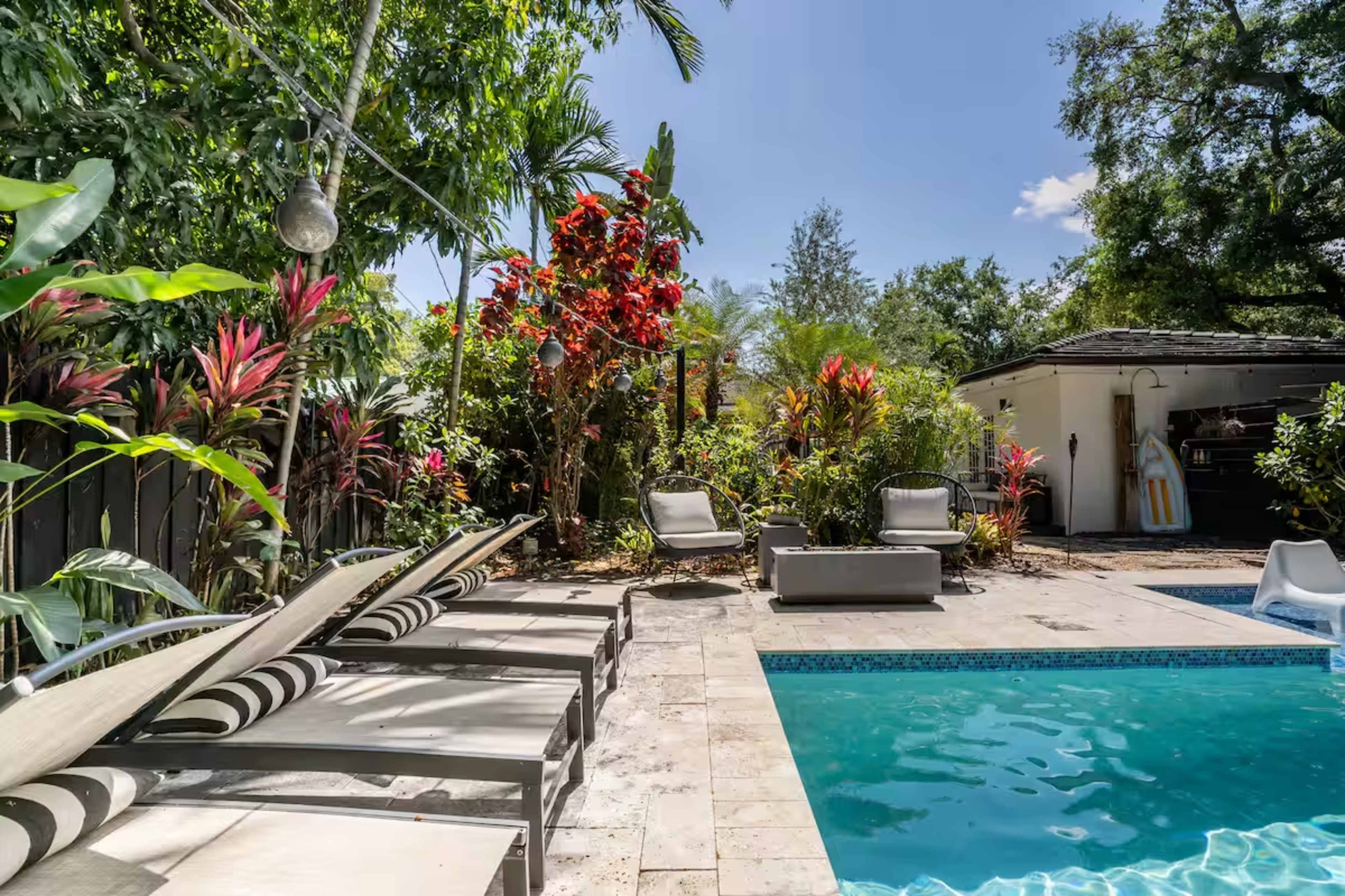 The image depicts a sunny backyard with a swimming pool, lounge chairs, and various tropical plants surrounding the area.