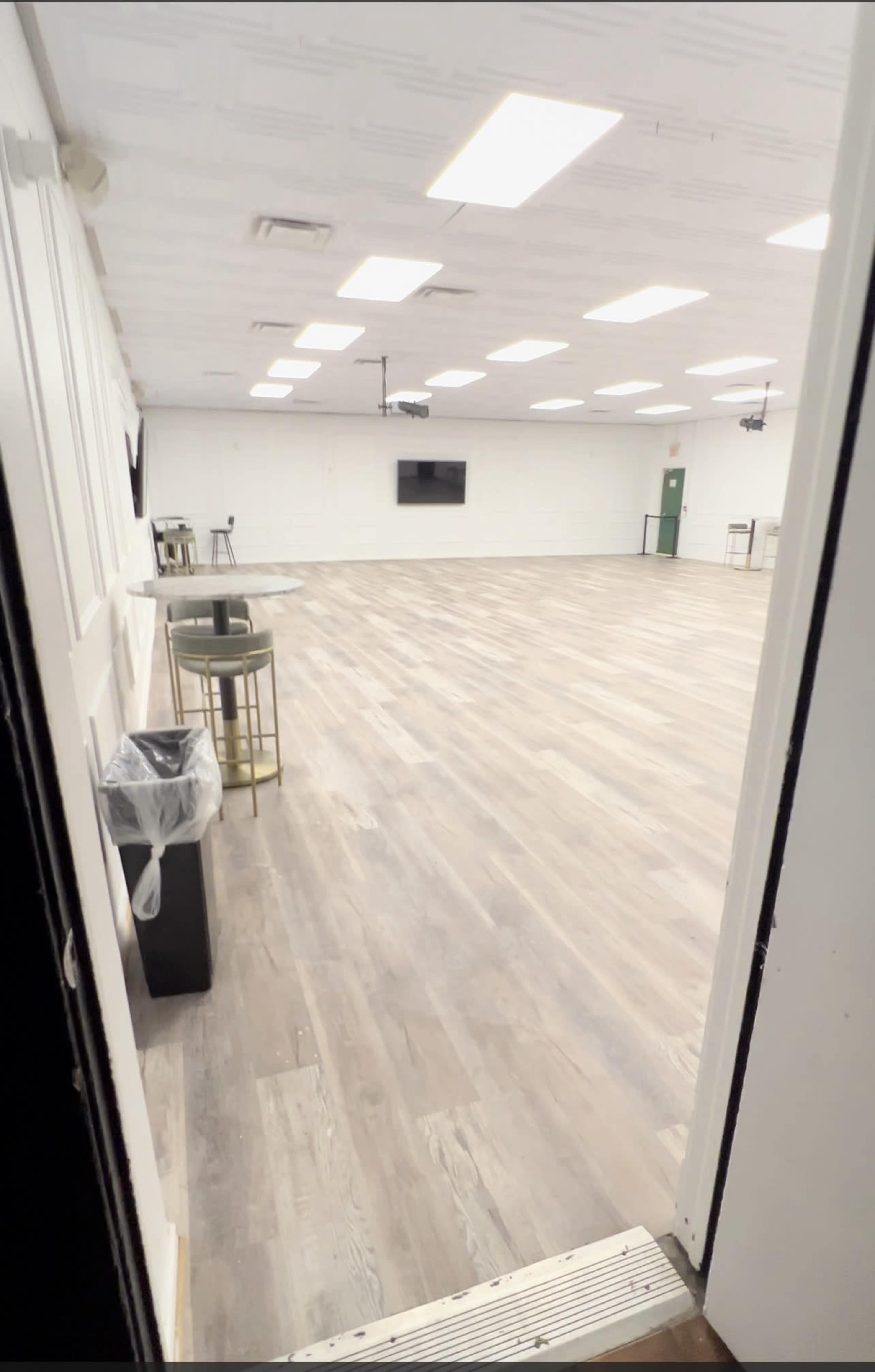 A vacant, well-lit room with a wooden floor and minimal furnishings, viewed from an open door.