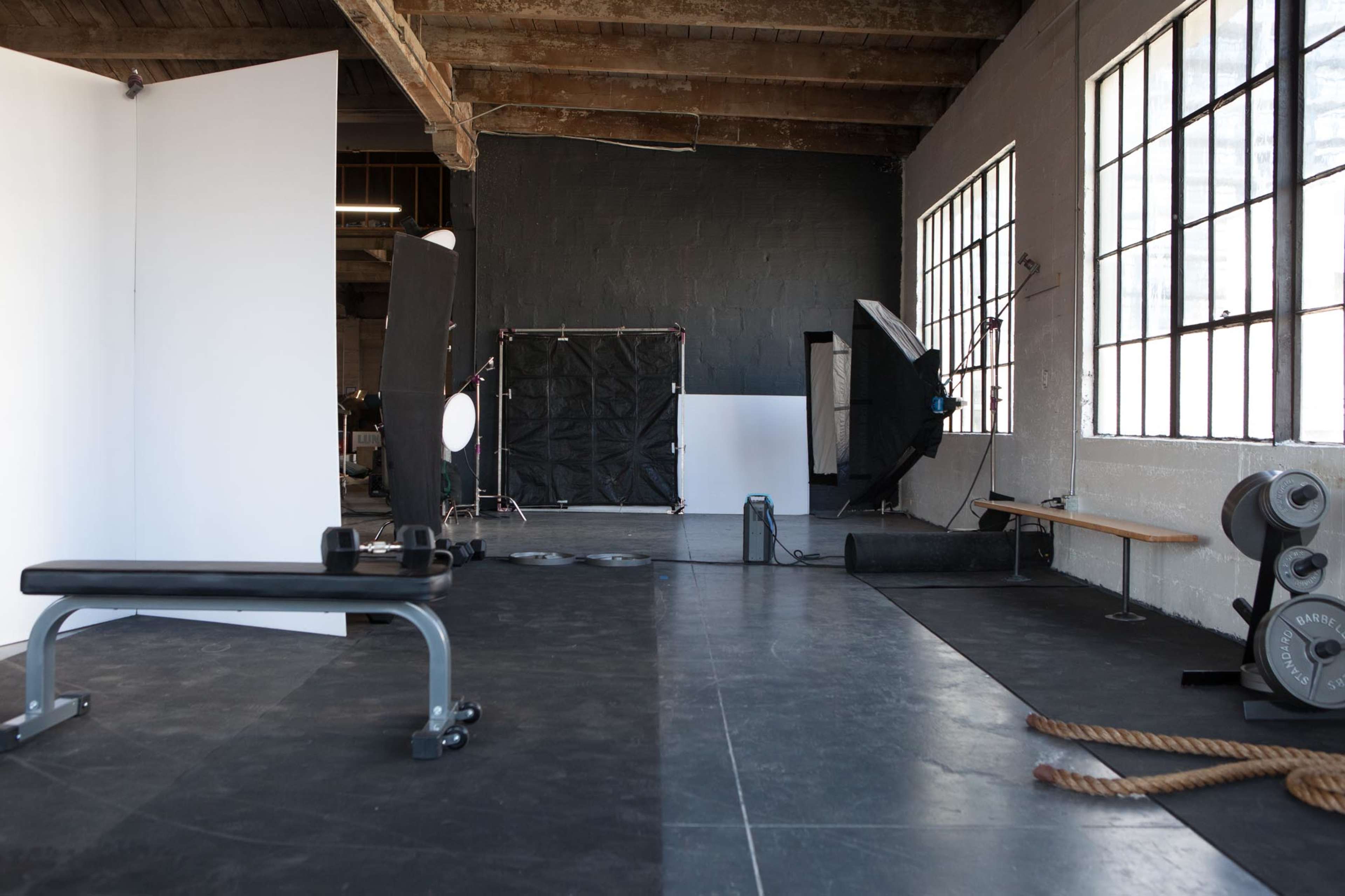 A gym or studio space with a weight bench, gym equipment, and large windows providing natural light.
