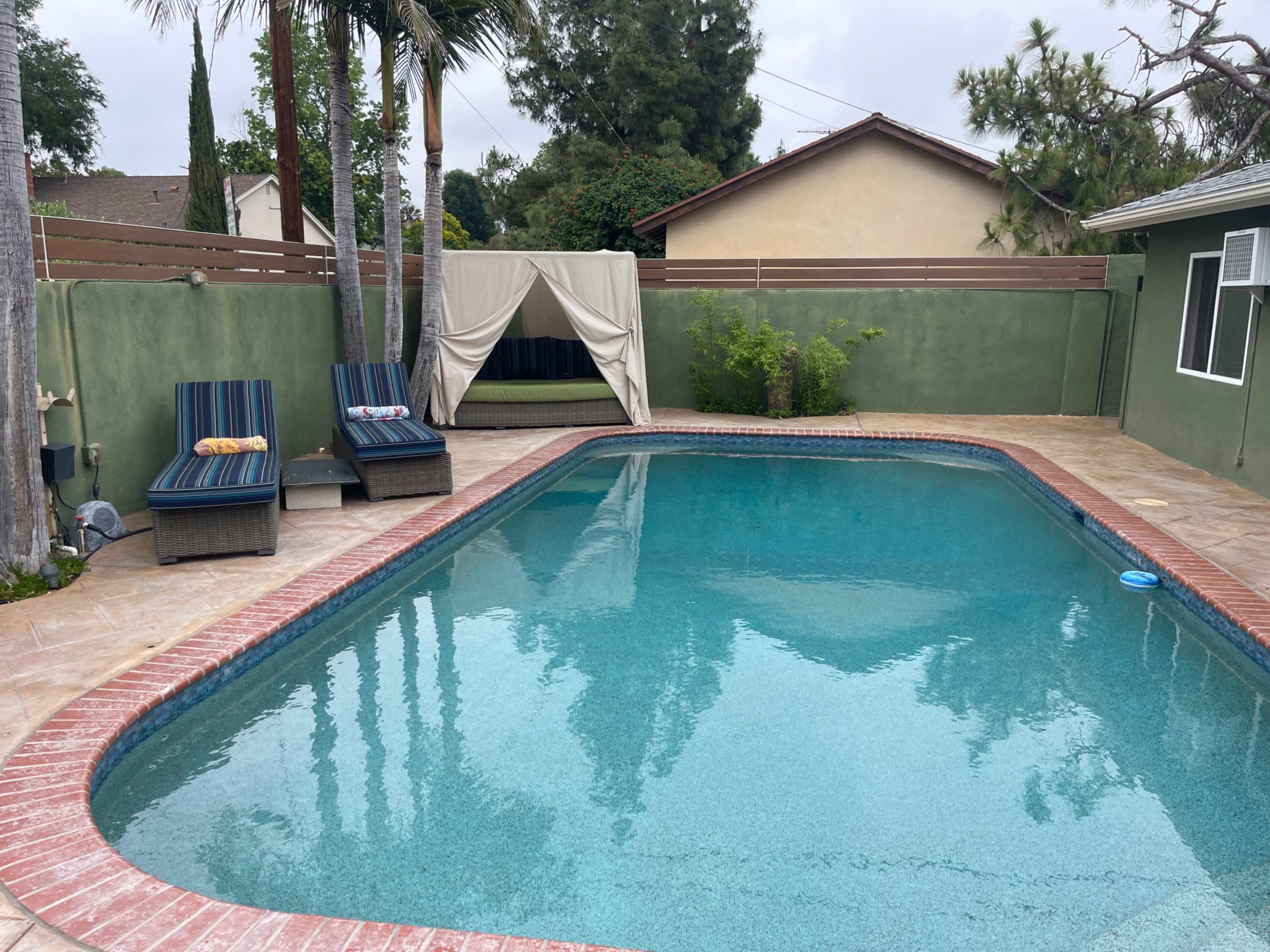 A swimming pool surrounded by loungers and a covered seating area in a backyard setting.