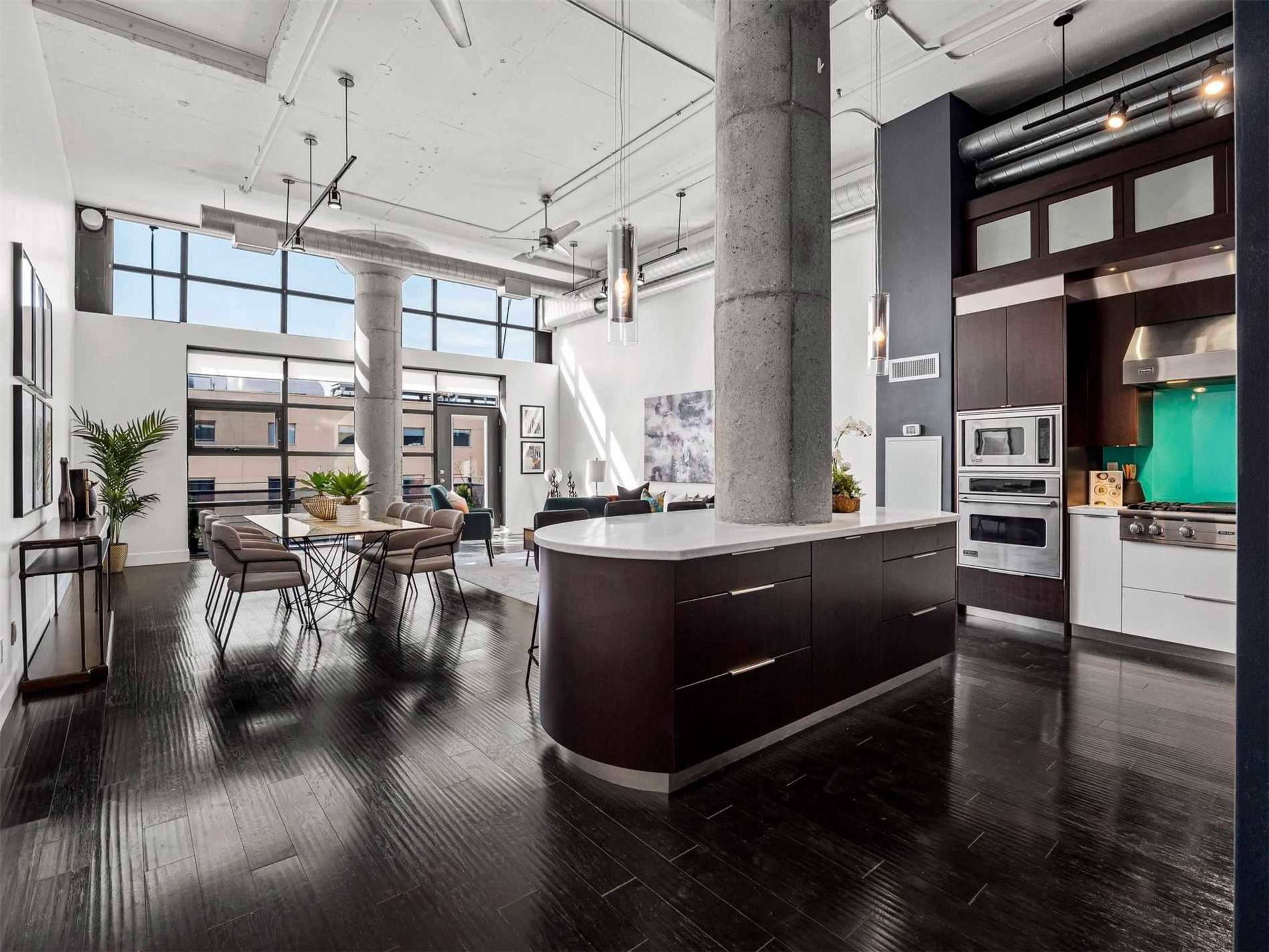 The image shows a spacious, modern kitchen and dining area featuring large windows, a central island, and stylish furniture.