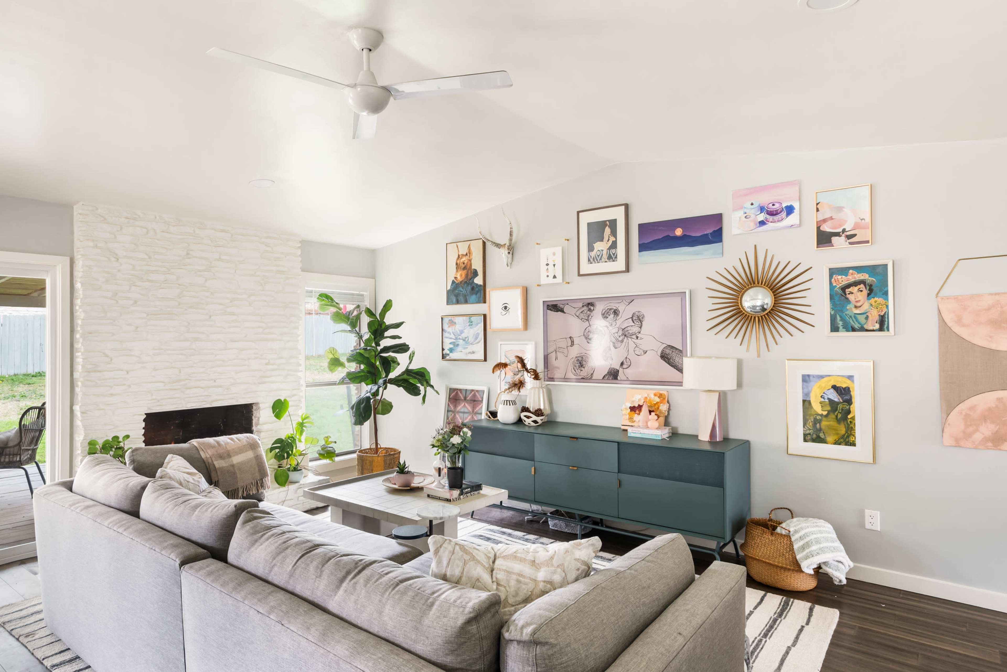A contemporary living room features a gray sectional sofa, a green media console, and a wall adorned with various framed artworks and photographs.