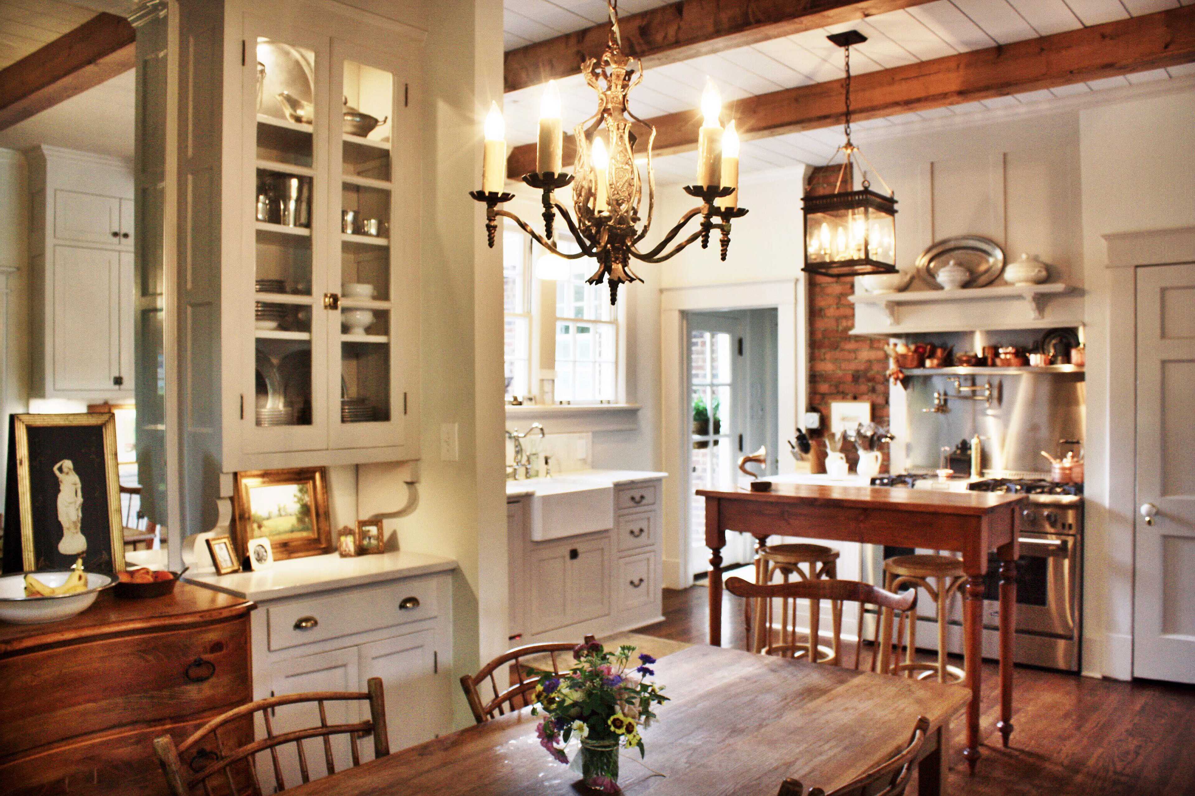 The image shows a well-lit kitchen and dining area featuring a wooden table with chairs, a chandelier, and a mix of modern and traditional decor.