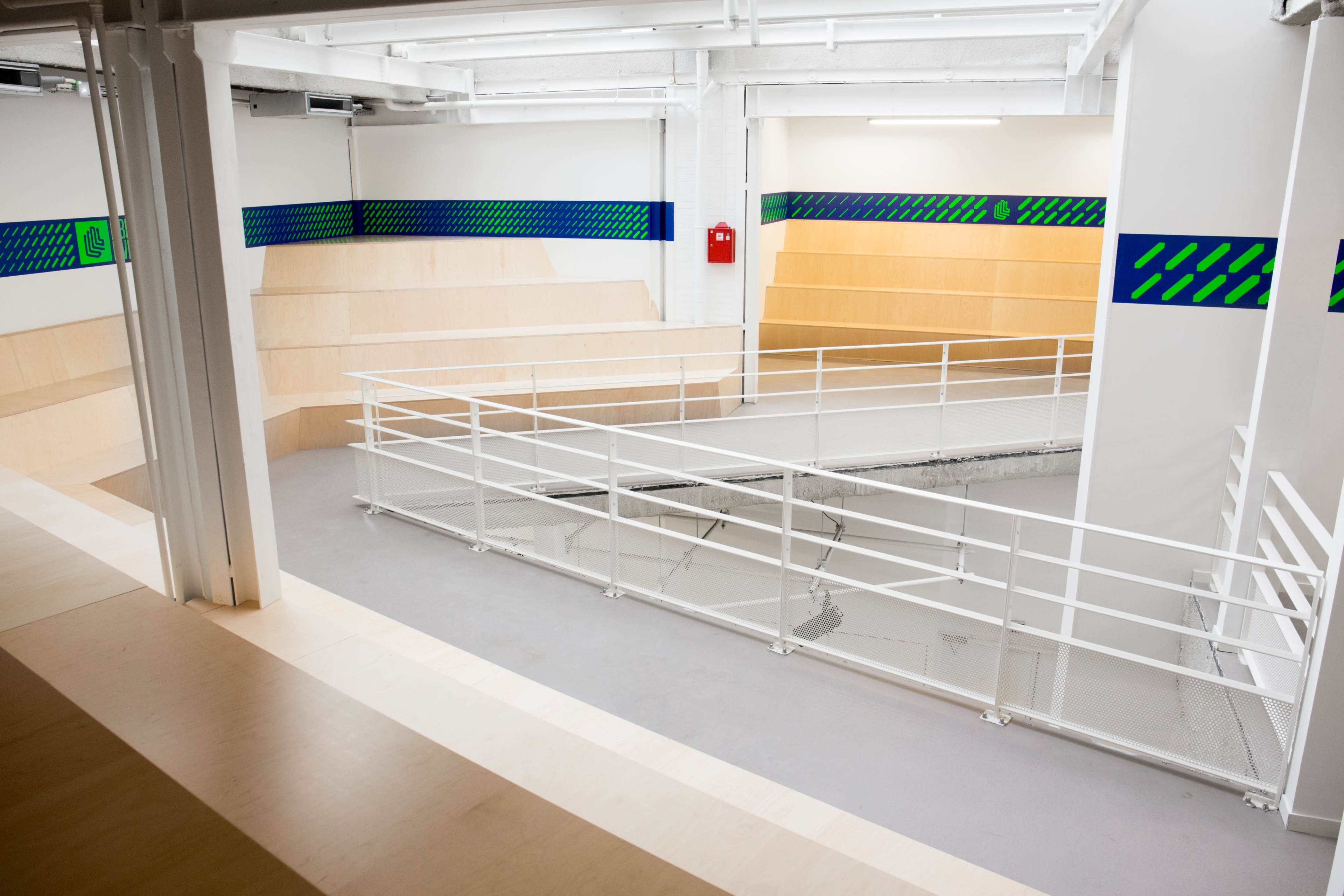 An indoor skatepark featuring wooden ramps, smooth flooring, and a railings around a circular area.