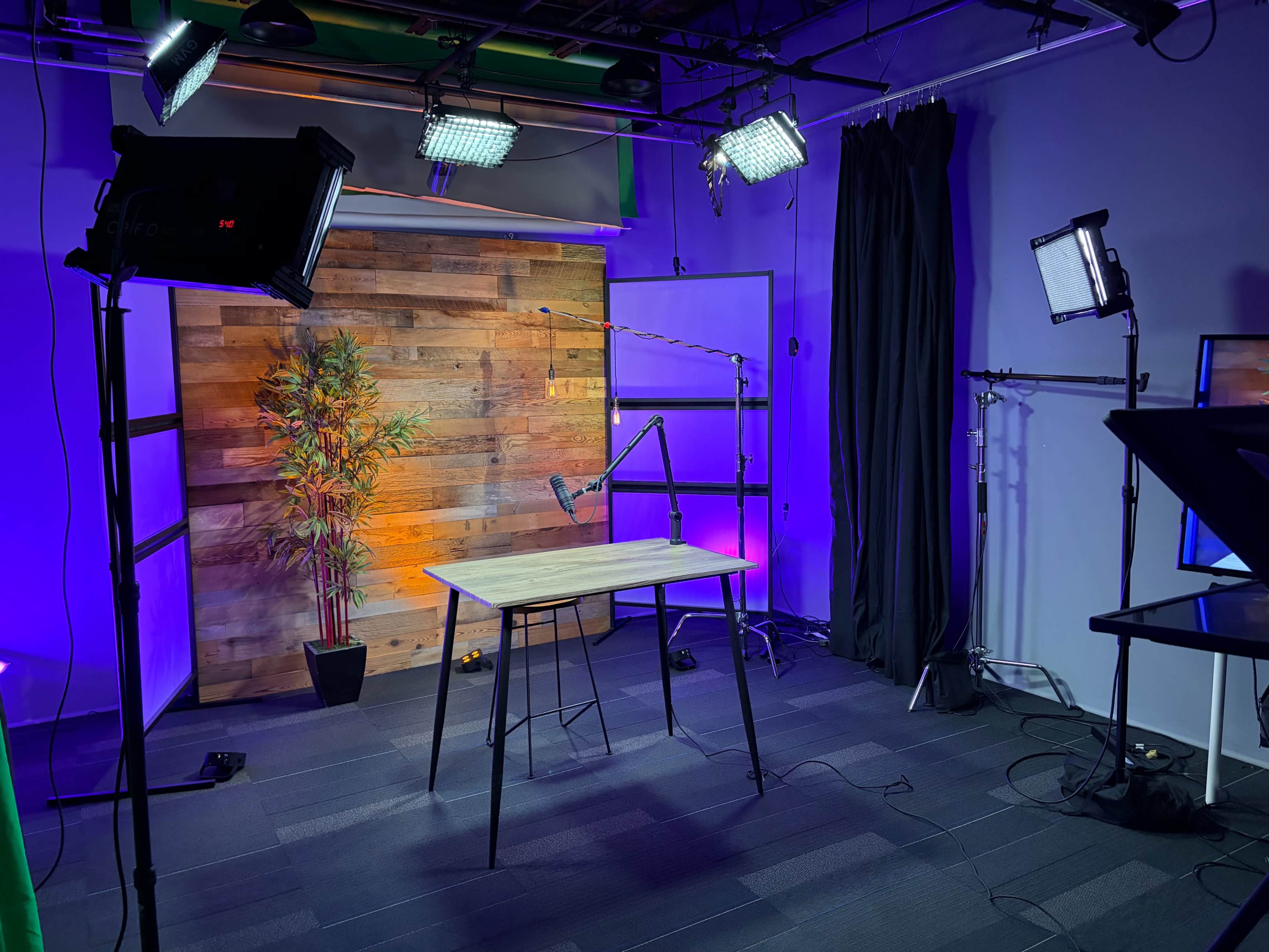 The image shows a studio setting with a wooden backdrop, a table in the center, and various lighting equipment positioned around the space.