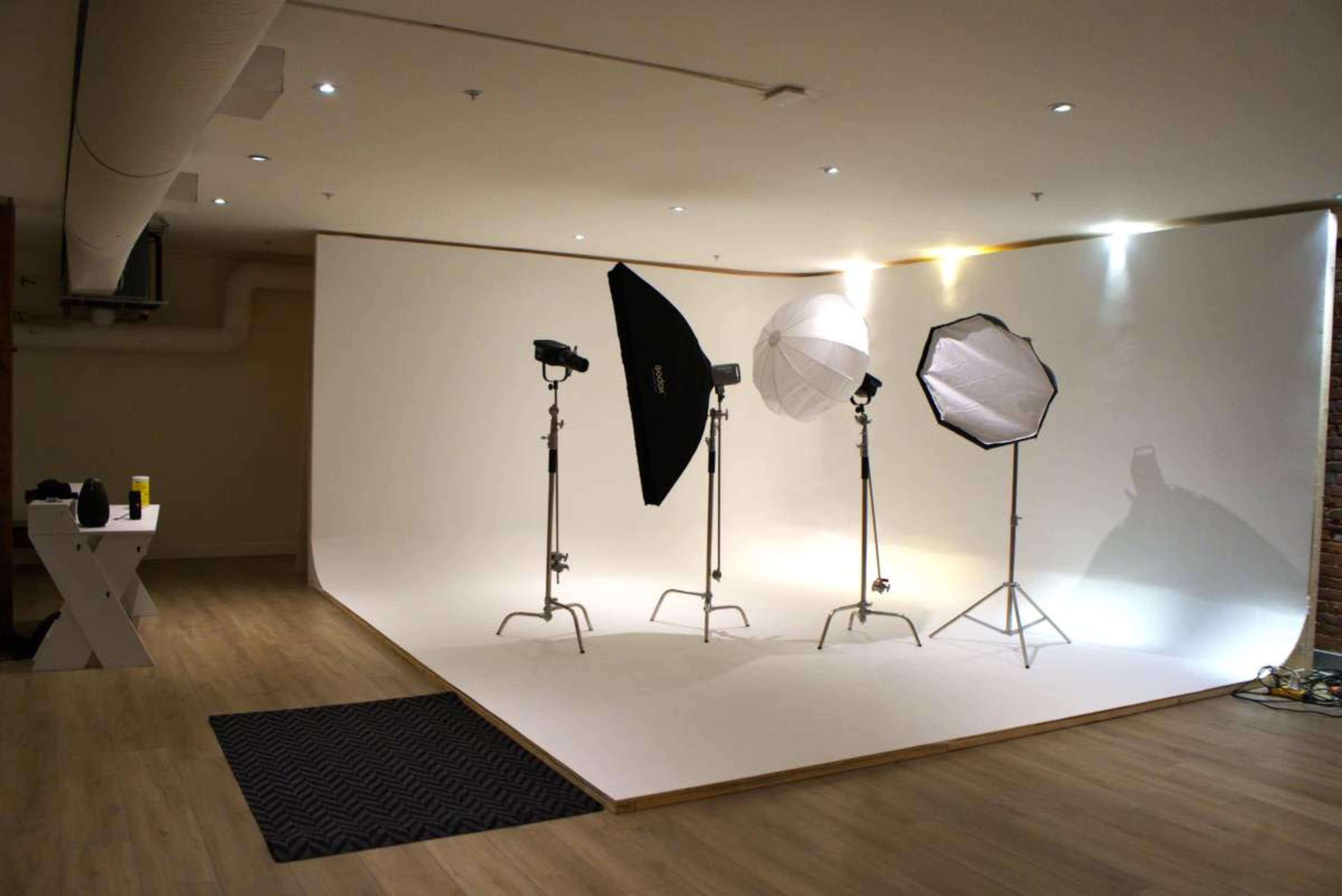The image depicts a photography studio with multiple light setups against a plain white backdrop.