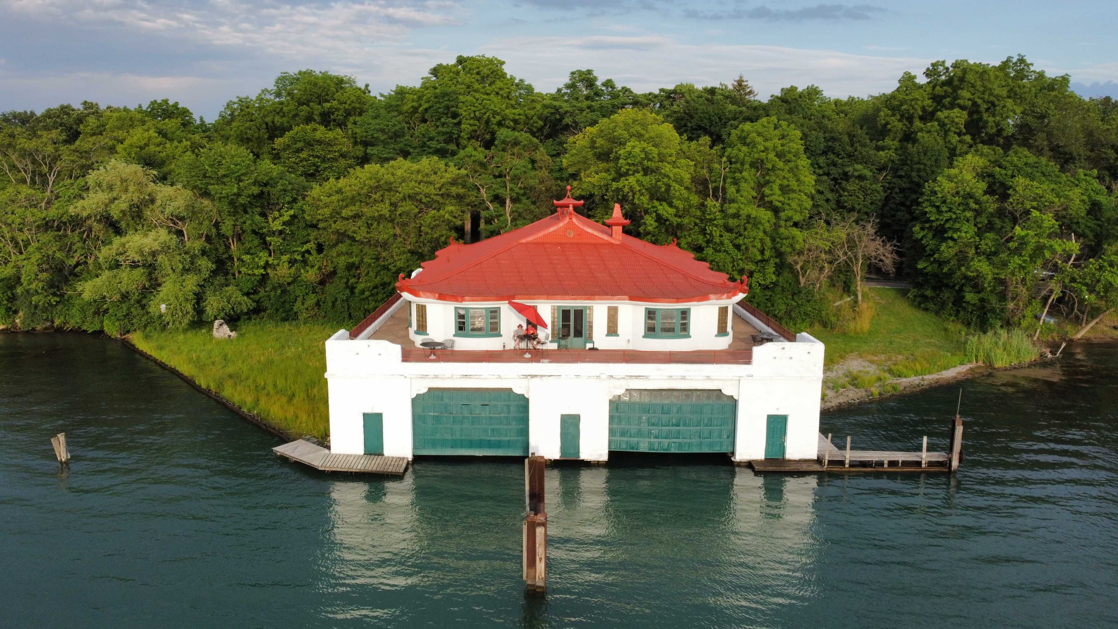 A structure with a red roof sits on stilts above water, surrounded by greenery.