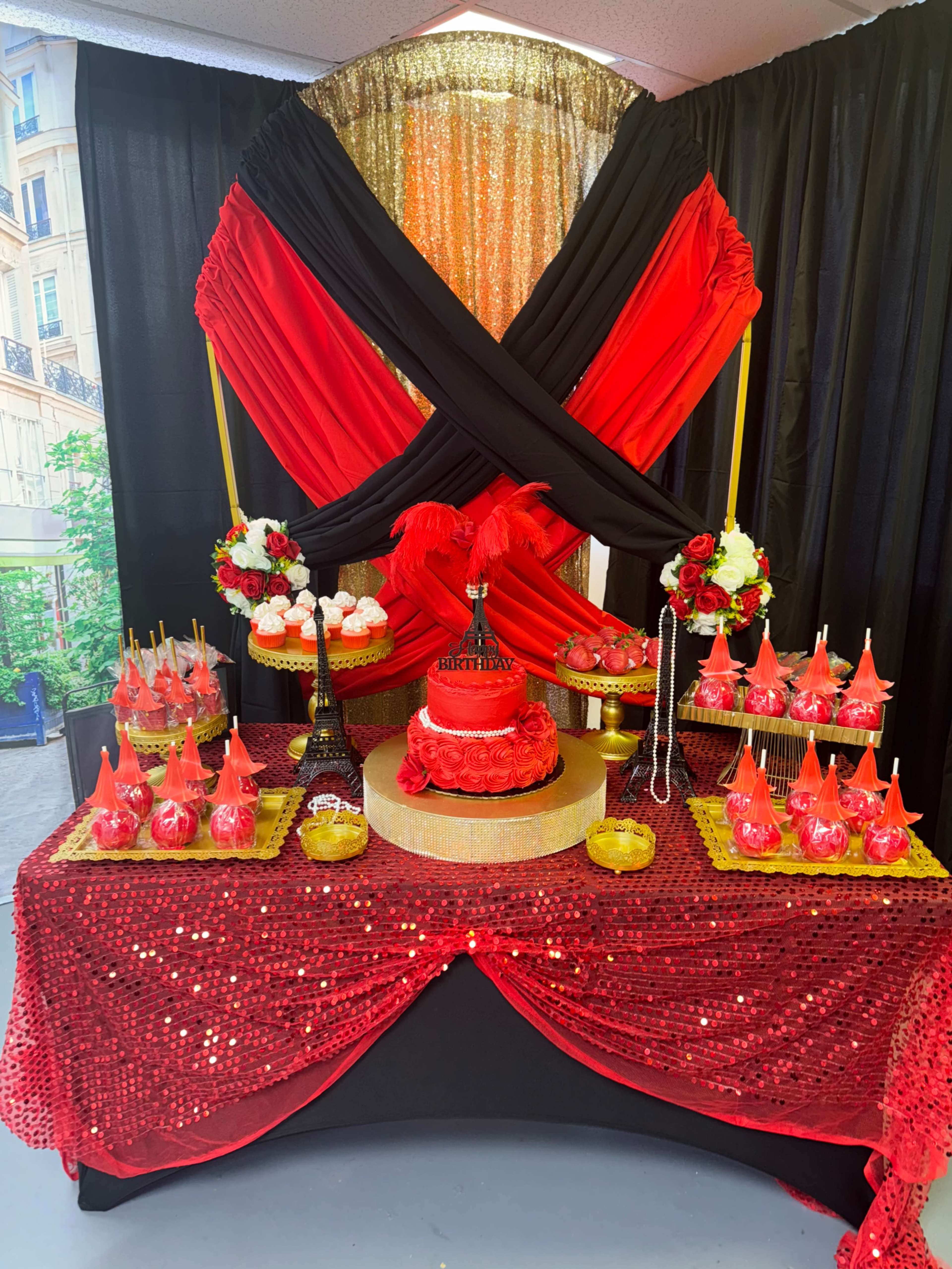 The image features a festive dessert table decorated with red and black drapery, showcasing a cake at the center, surrounded by various themed treats and decorations.