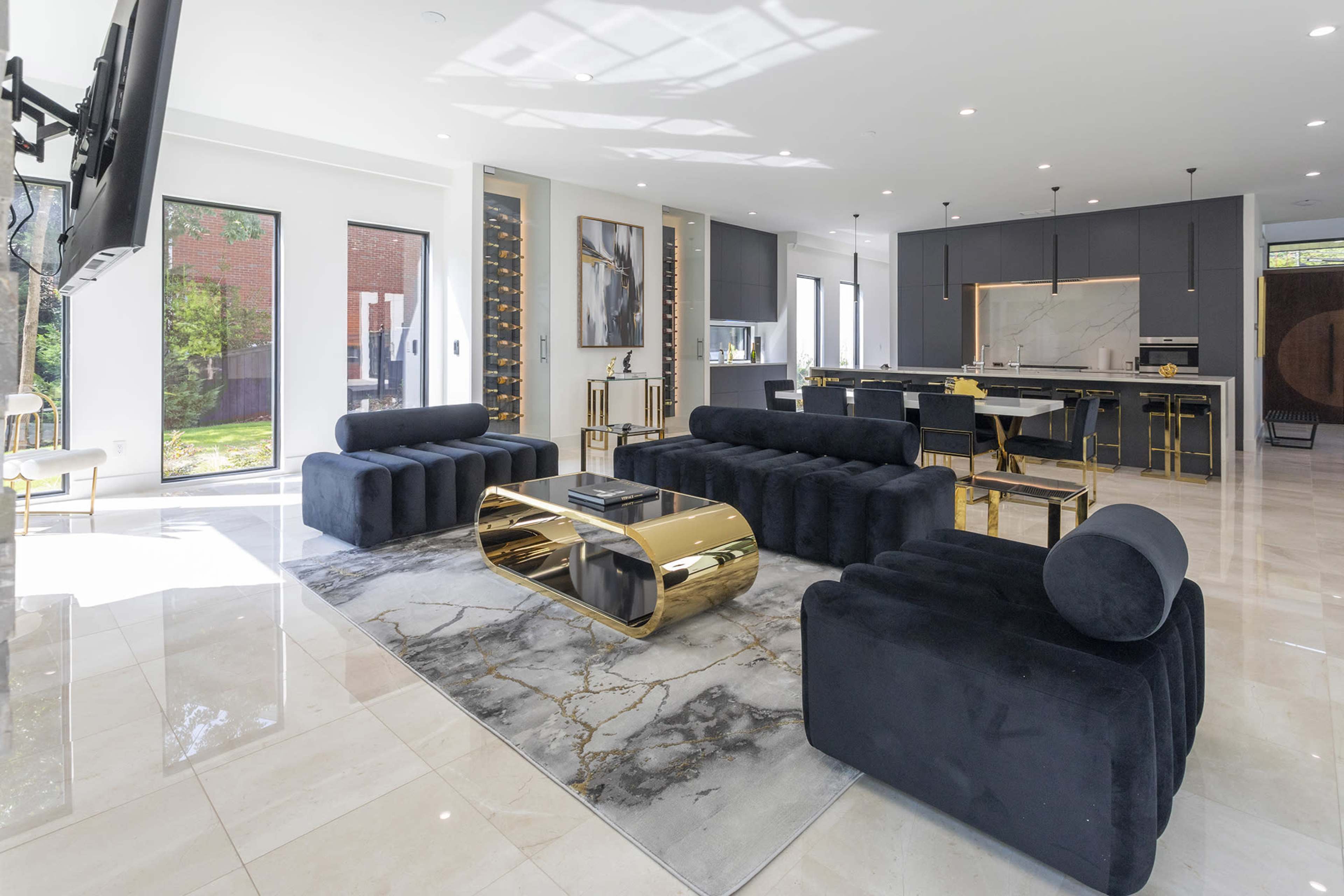 A modern living room with black upholstered furniture, a gold-accented coffee table, and a sleek kitchen in the background.
