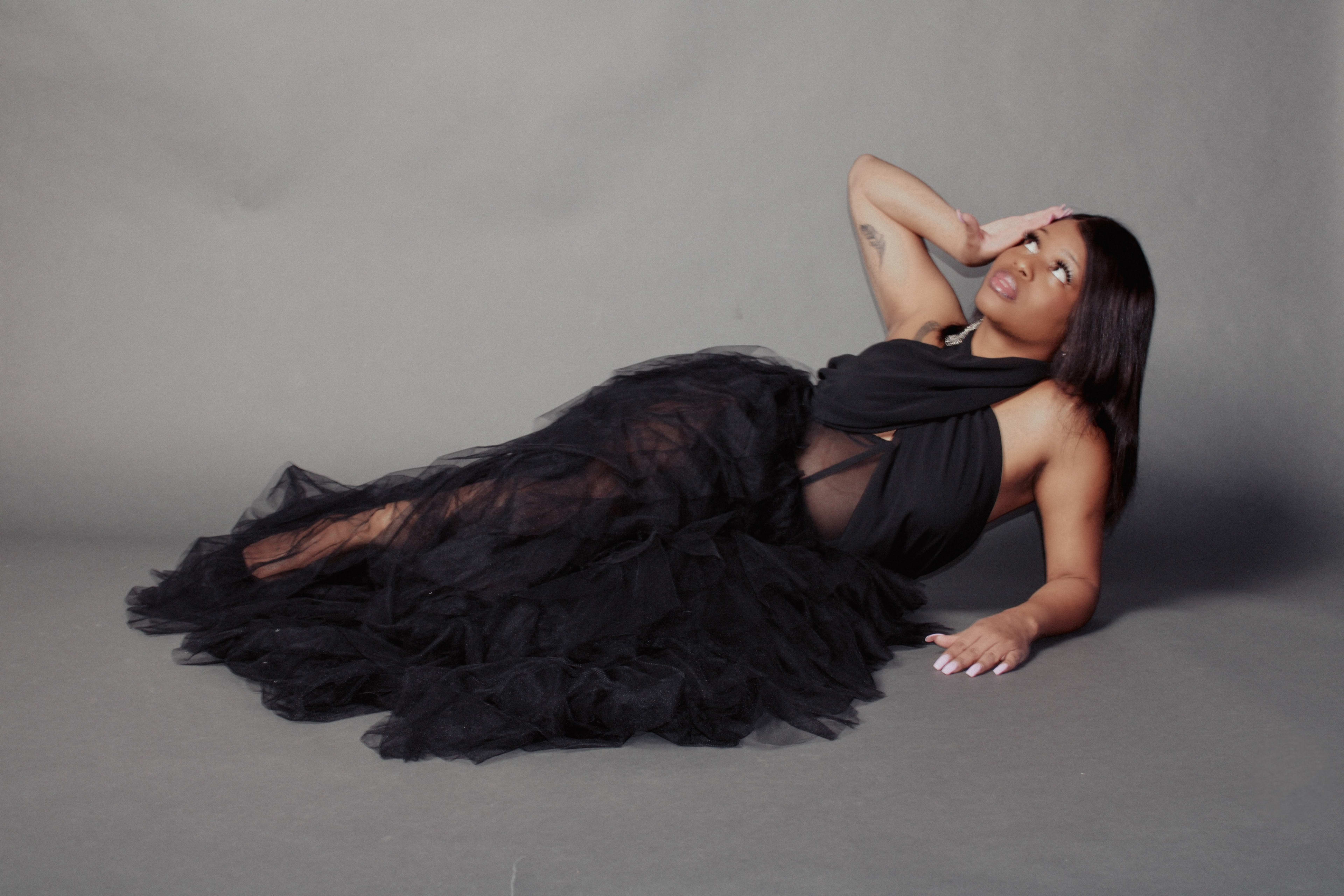 A fashion model in a black dress posing for a photoshoot on grey floors.