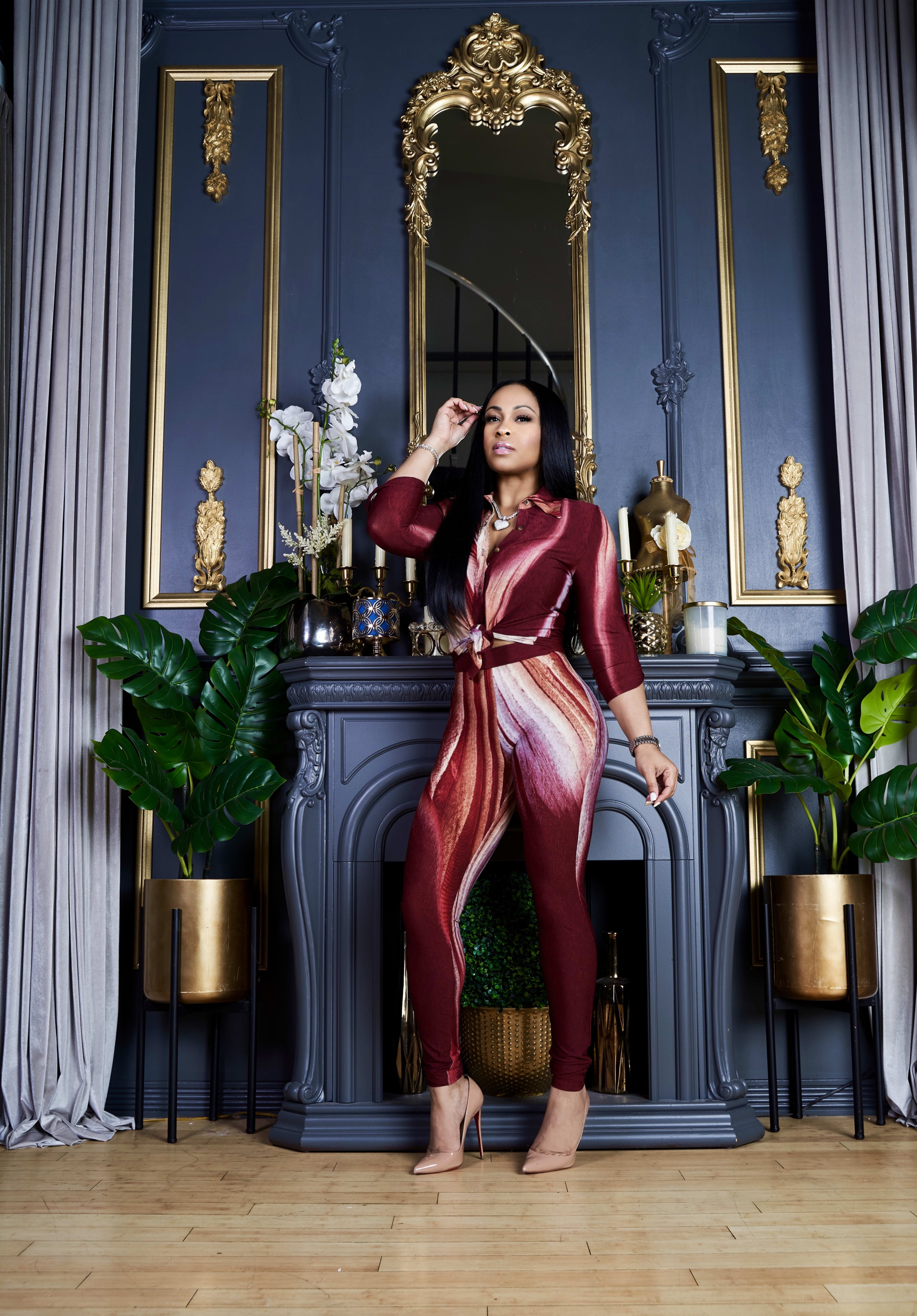 A fashion photoshoot featuring a woman standing in front of a blue and gold fireplace with plants.