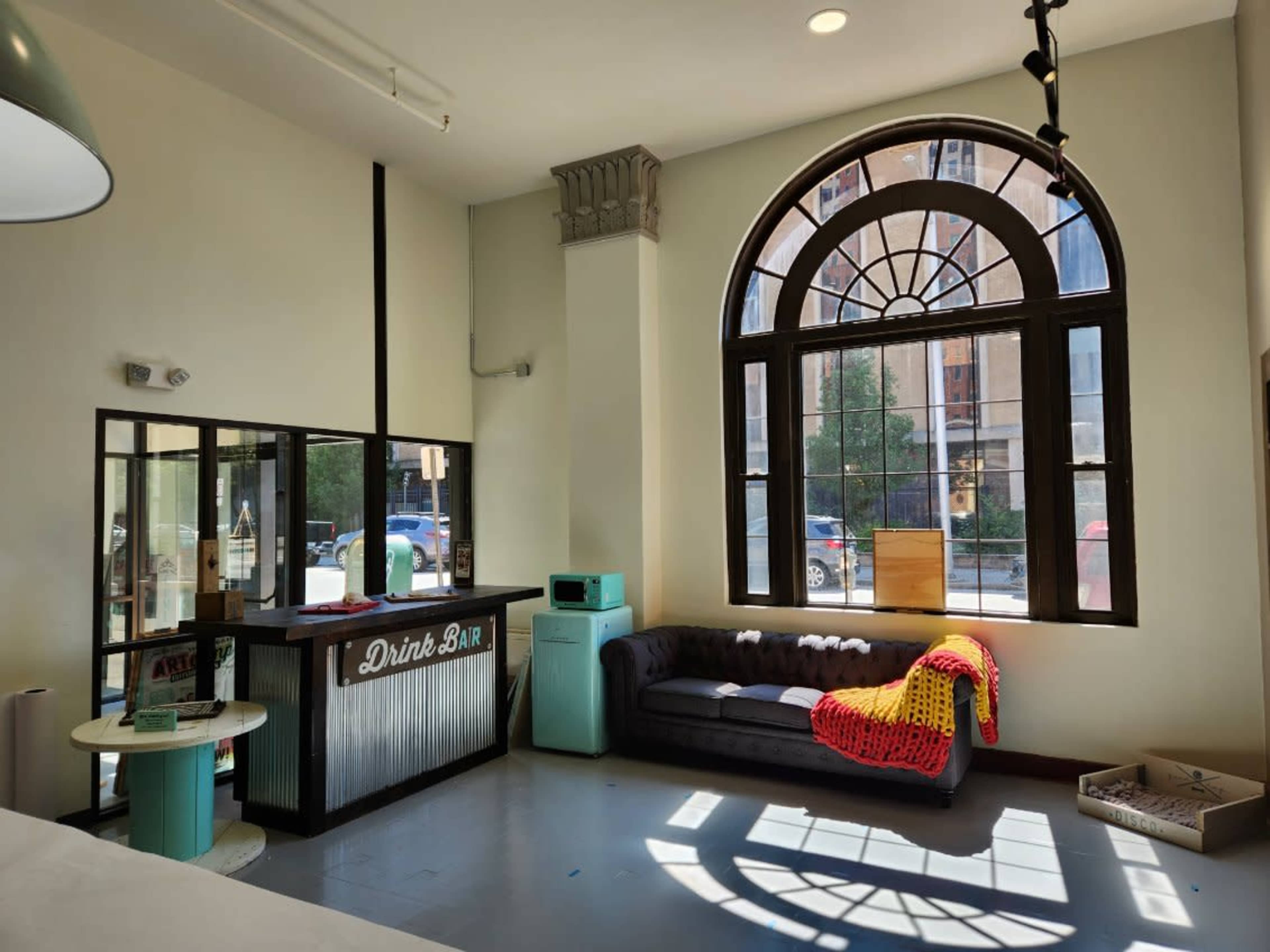 The interior features a drink bar next to a large arched window, with a couch draped in a colorful blanket facing the street.