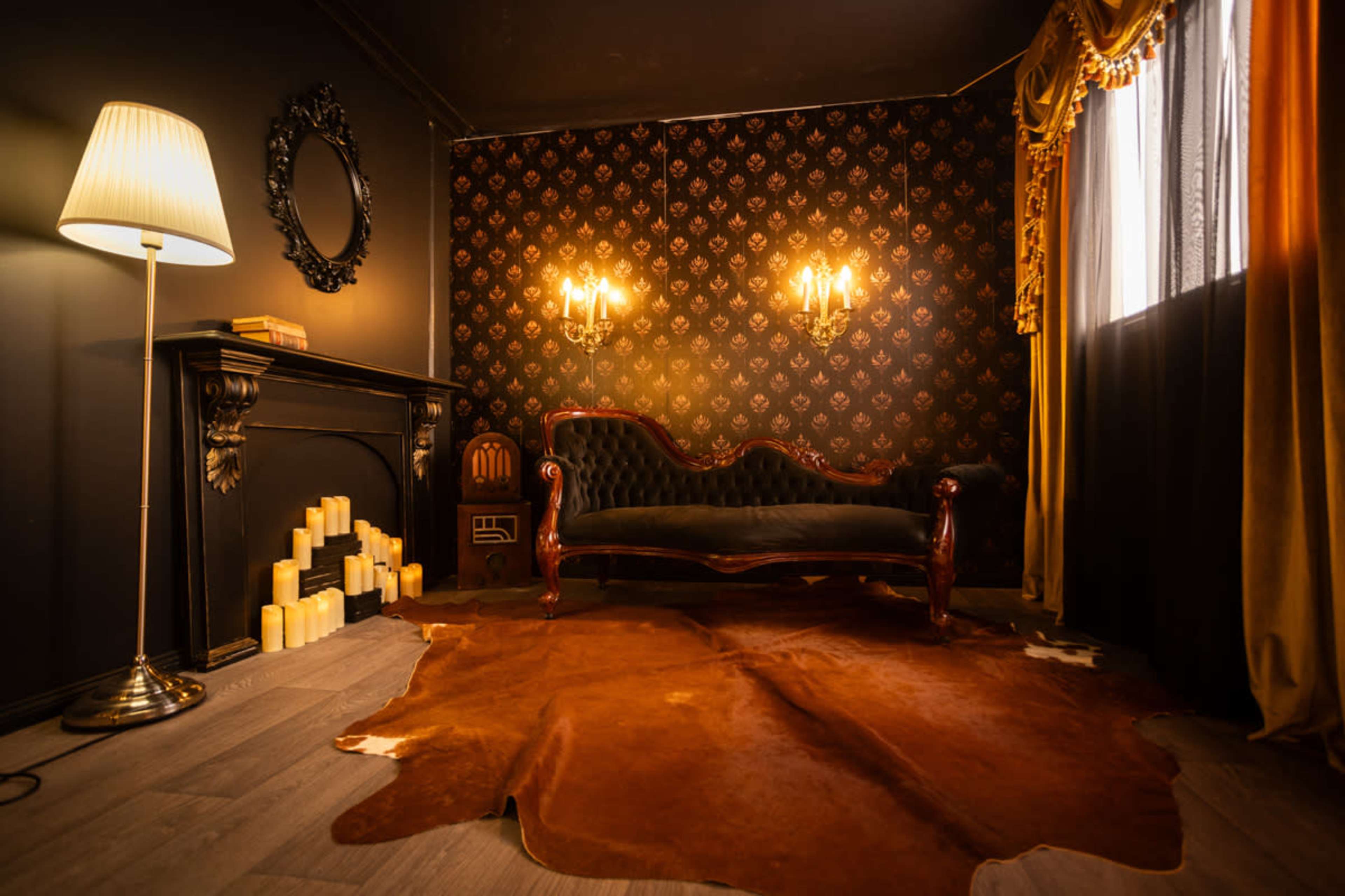 The image shows a dimly lit room with a vintage-style sofa, a decorative mirror, and a fireplace adorned with candles.