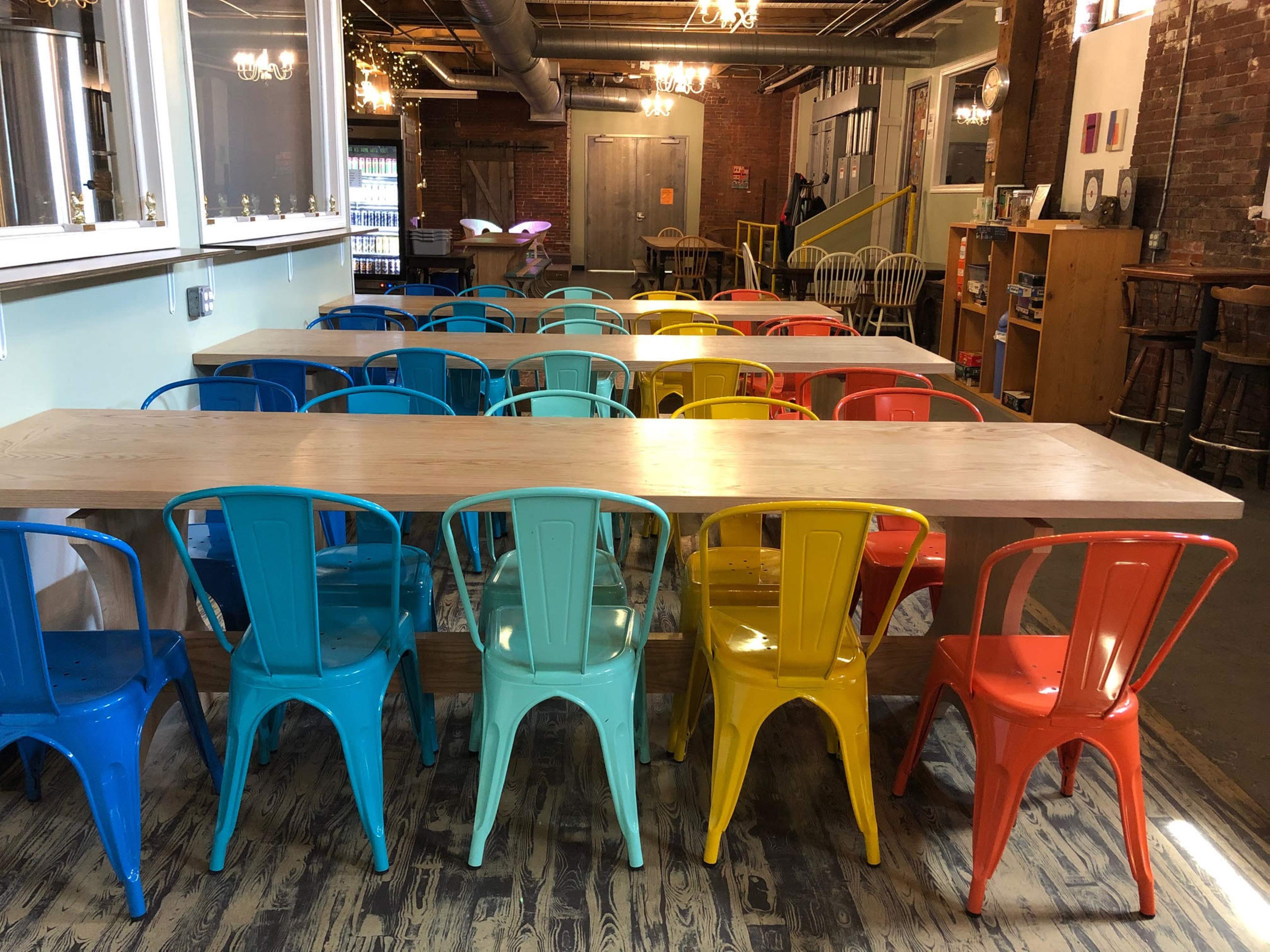 A long wooden table is surrounded by brightly colored metal chairs in a modern indoor space.