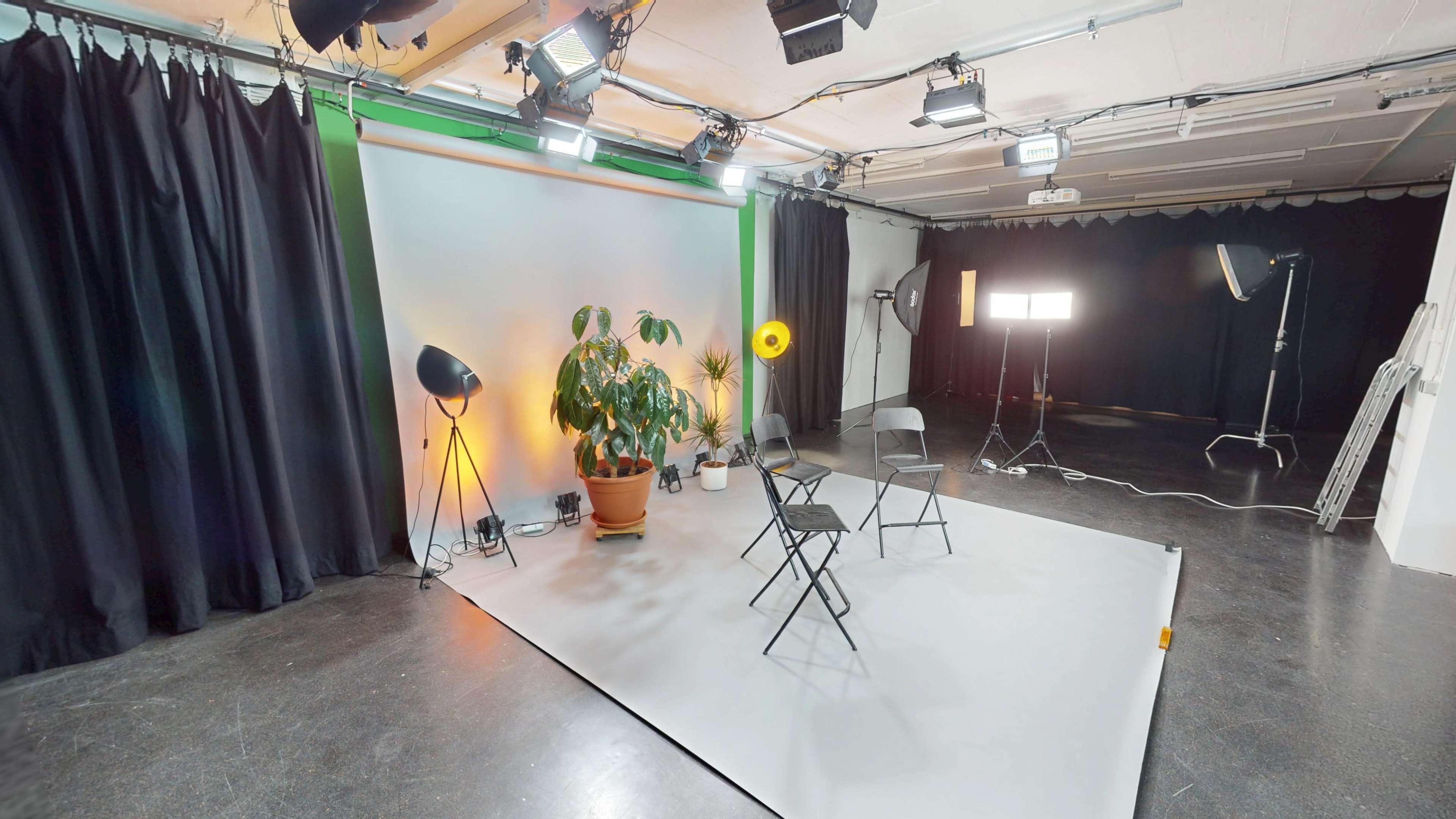 The image shows a photography studio with two empty chairs, a potted plant, and various lighting equipment set up against a colorful backdrop.