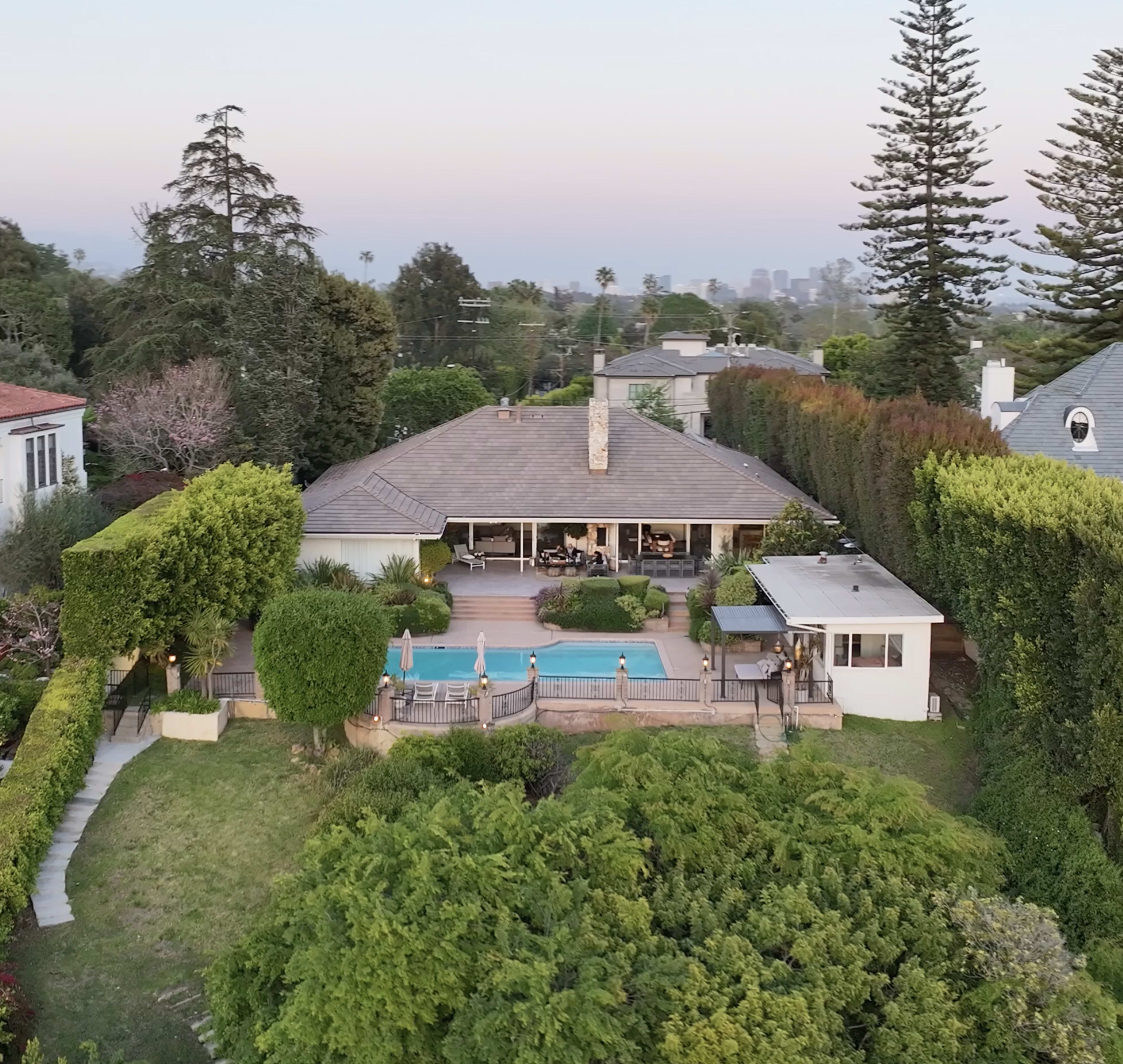 A spacious residential property features a backyard with a swimming pool, surrounded by lush greenery and tall trees.