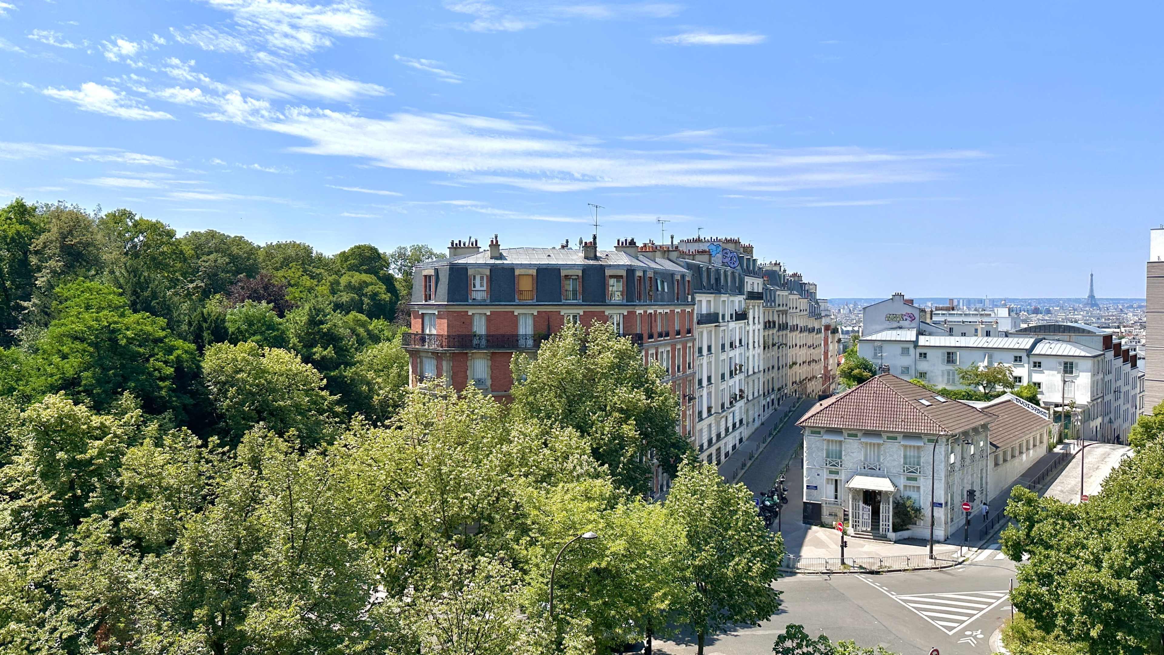A cityscape featuring tree-lined streets and buildings, with a clear blue sky in the background.