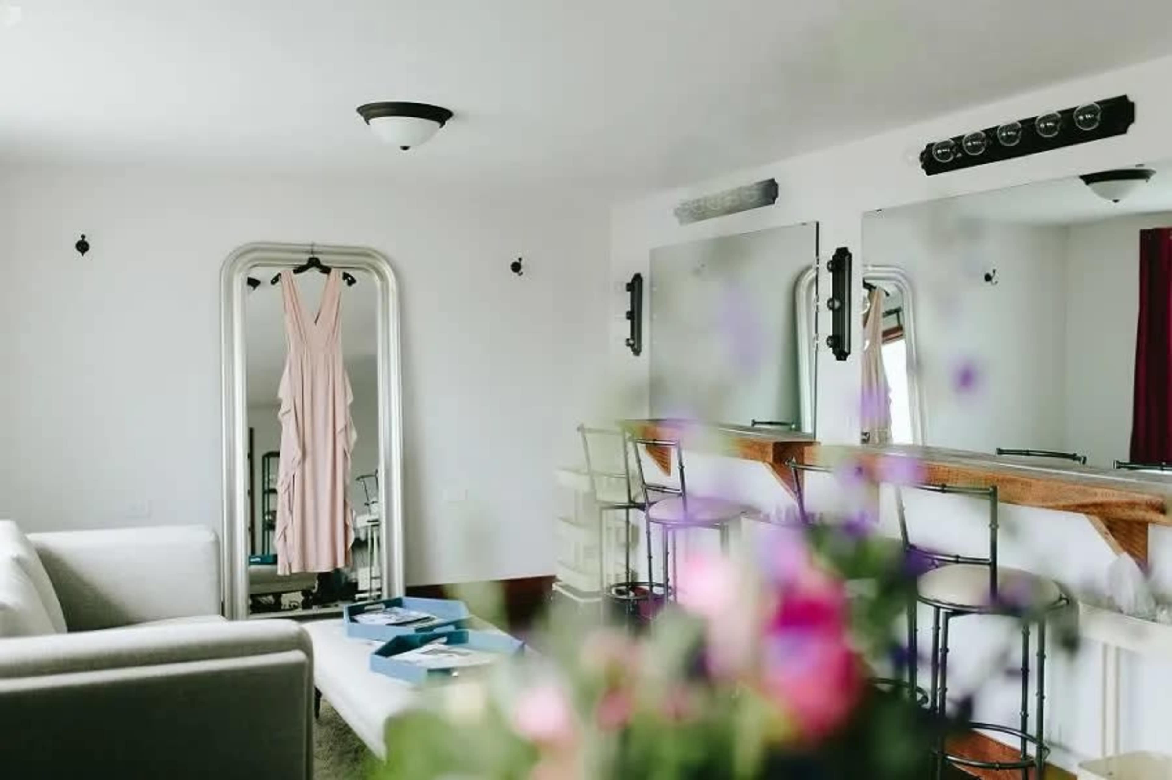 A bright room with a cream-colored dress hanging on a mirror in front of a small bar area and a couch.