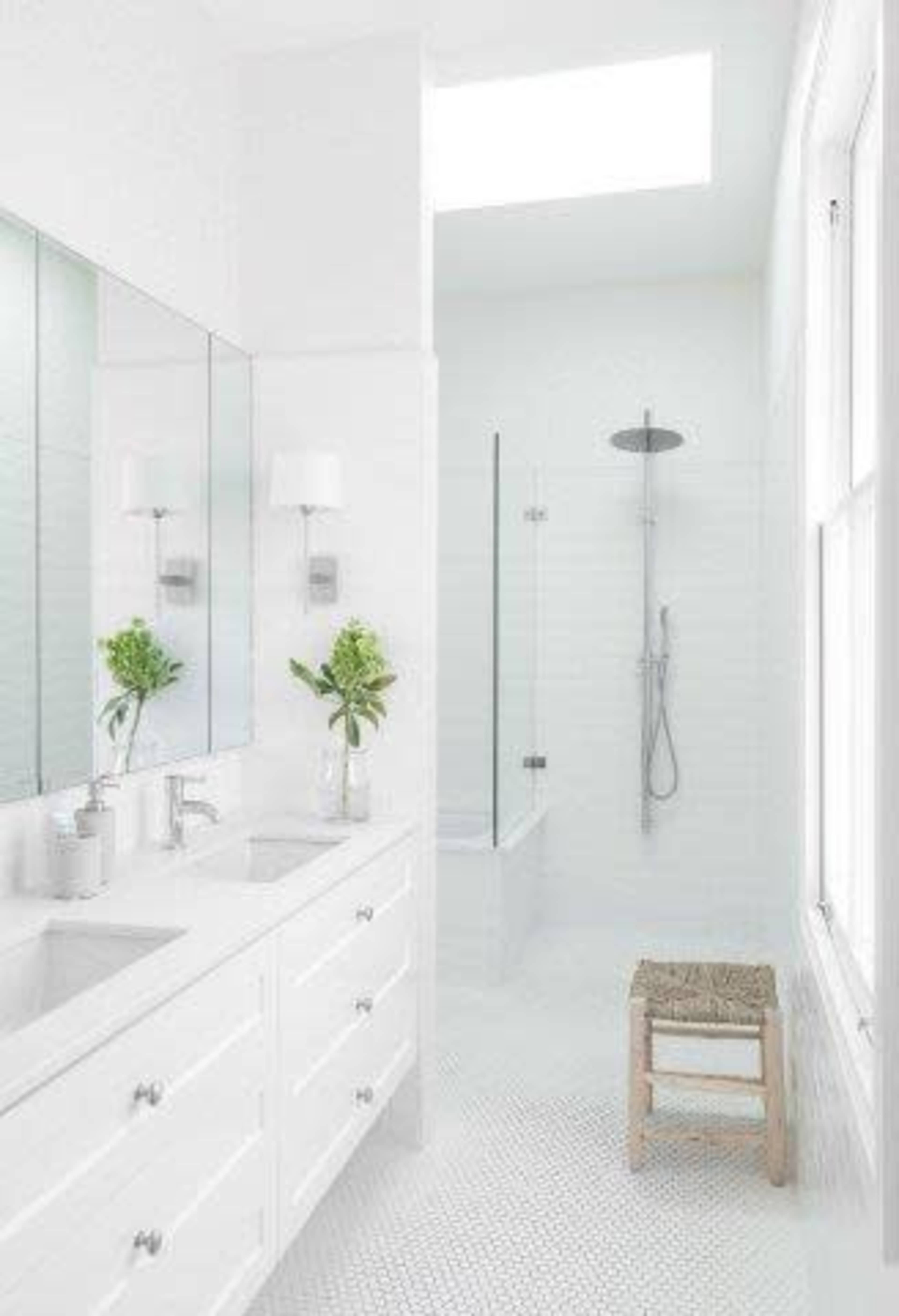 A bright, modern bathroom features a double sink vanity, a glass-enclosed shower, and a skylight.