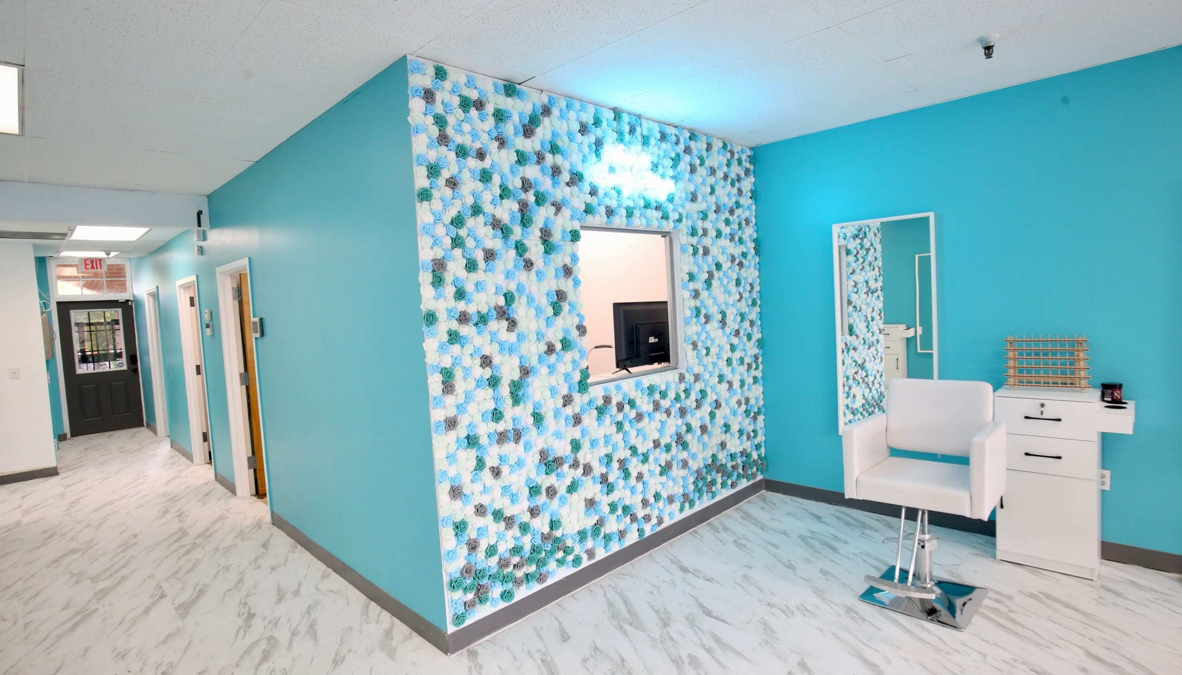 A brightly colored room with a turquoise wall featuring a decorative panel and a white vanity area, including a chair and mirror.