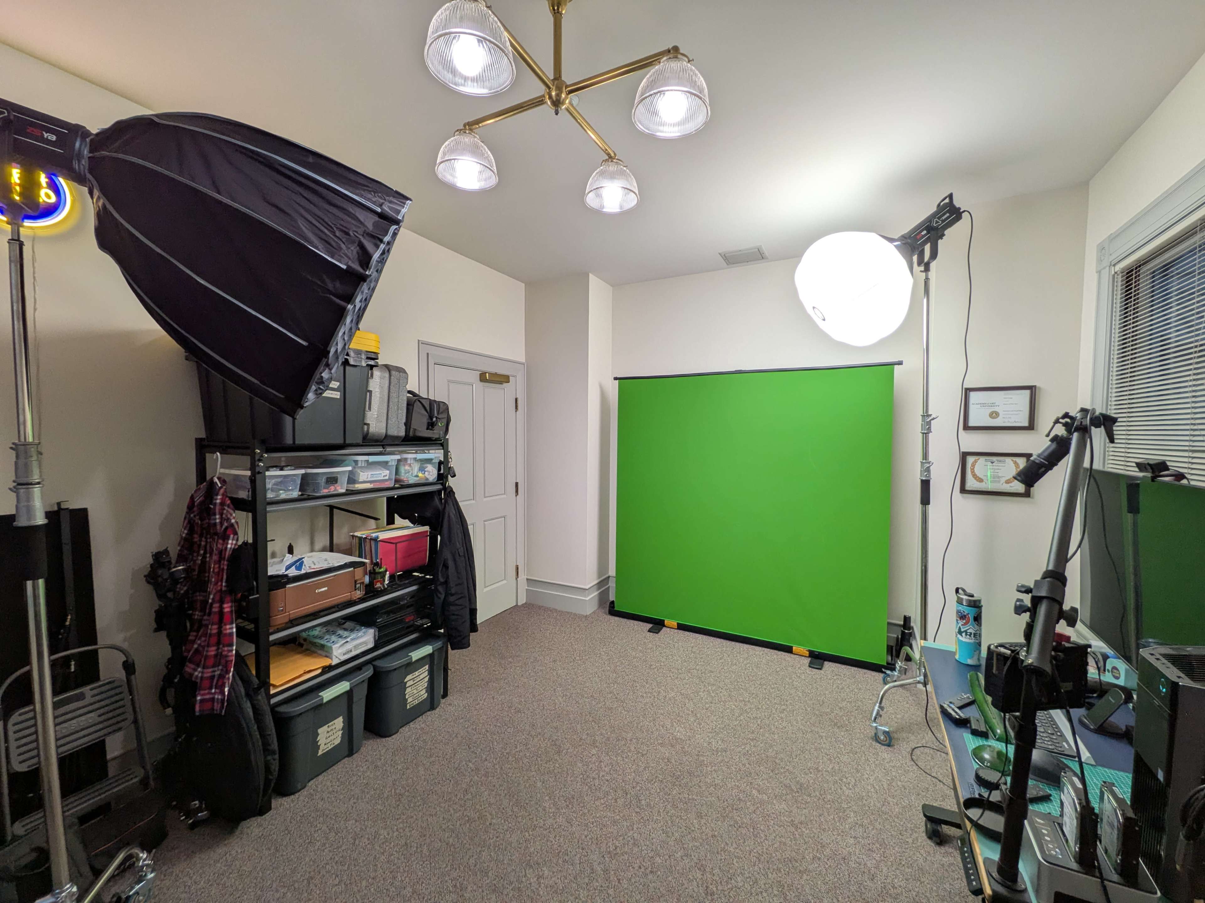 The image shows an indoor studio setup featuring a green screen, lighting equipment, and storage shelves filled with various items.