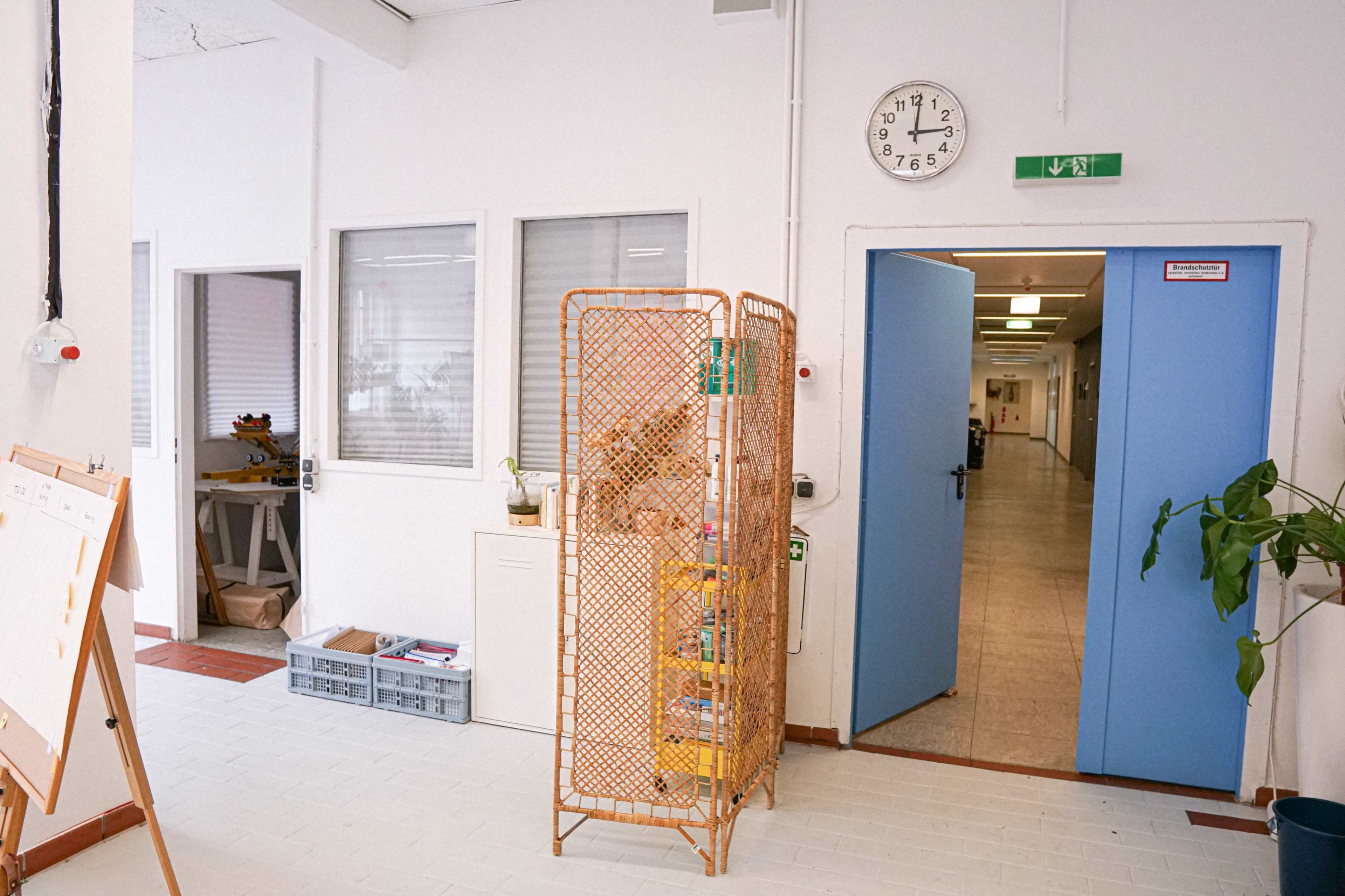 The image shows a hallway in a building with light blue doors, a clock on the wall, and a decorative partition containing items.