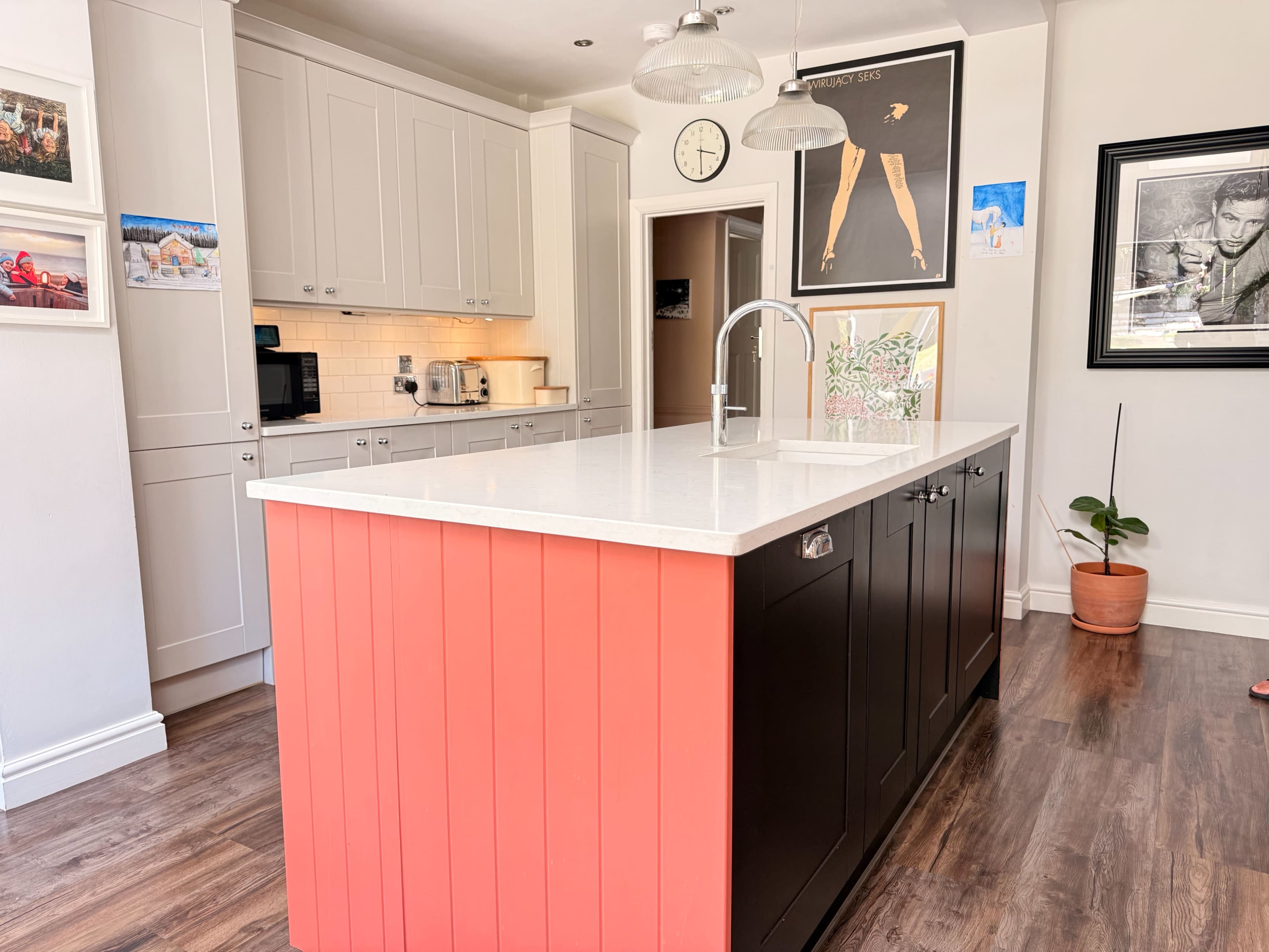 The image shows a modern kitchen featuring a central island with a two-tone design, light gray cabinets, and a white countertop.