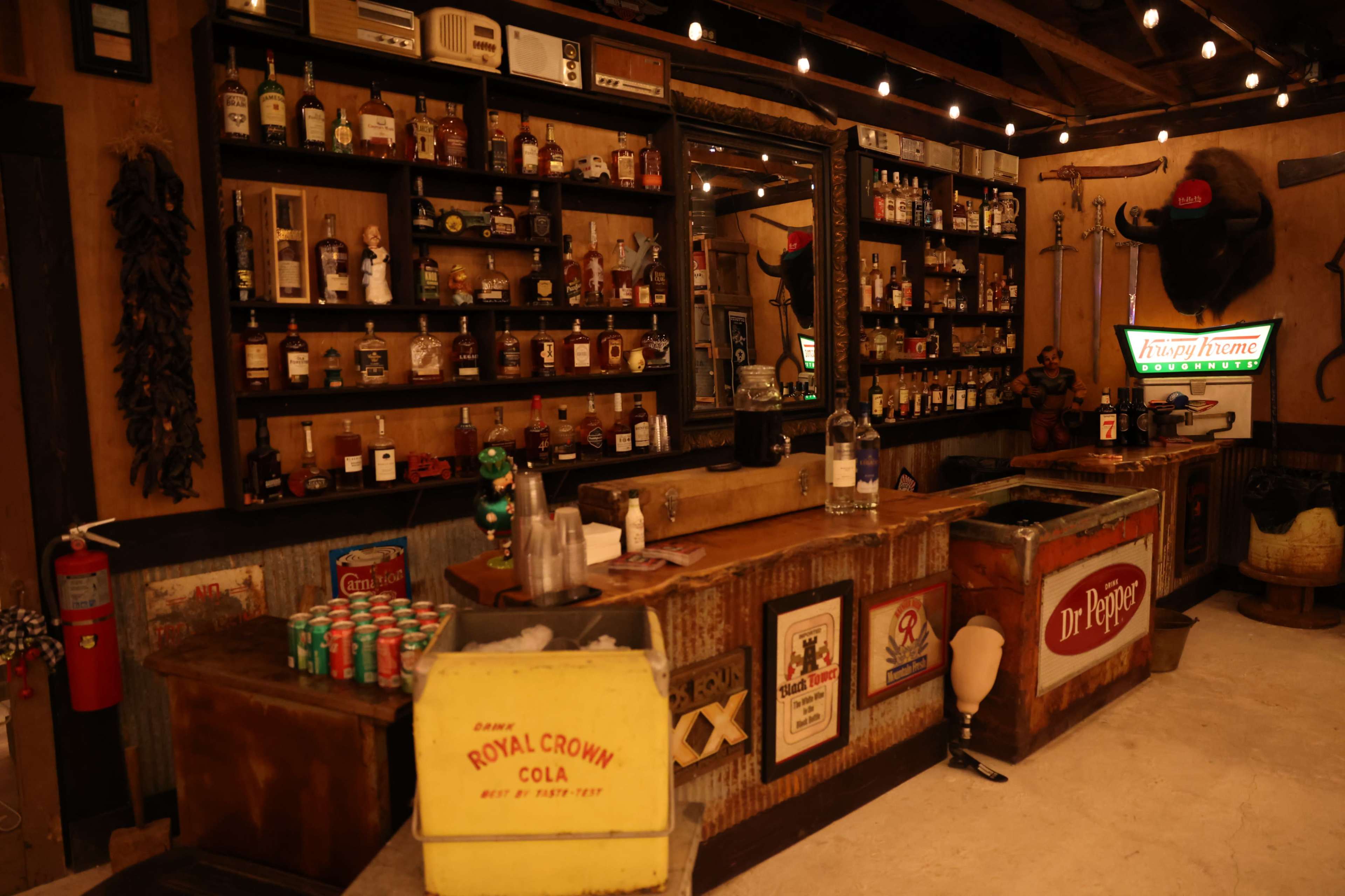 A rustic bar interior with shelves filled with various liquor bottles, vintage signs, and a wooden counter.